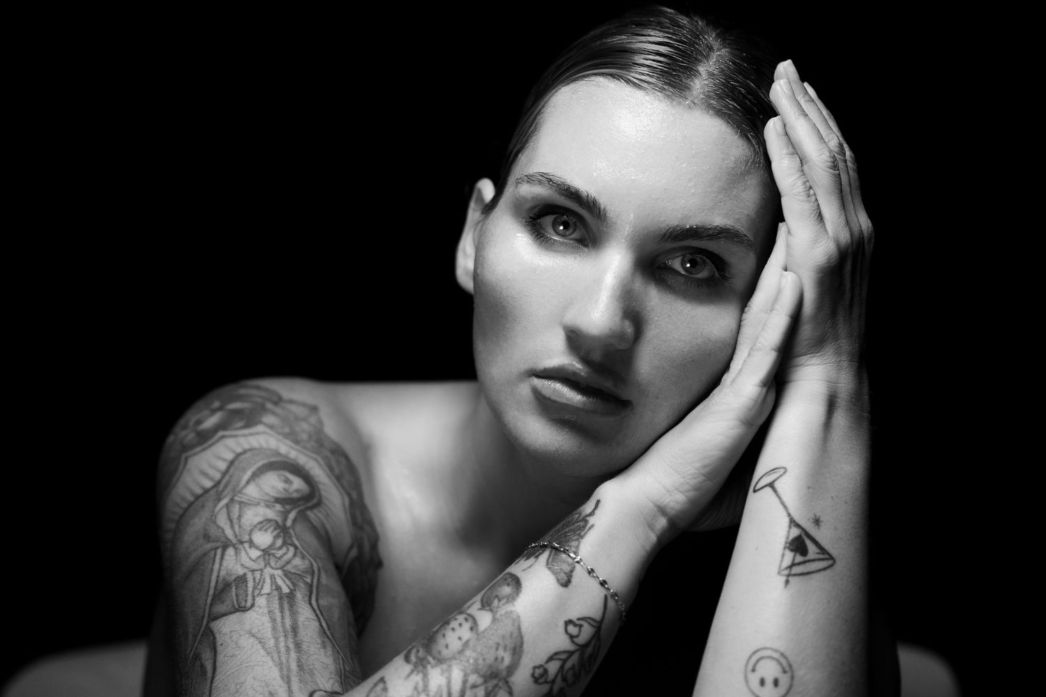 Black and white close-up portrait showcasing tattooed arms and dramatic lighting.