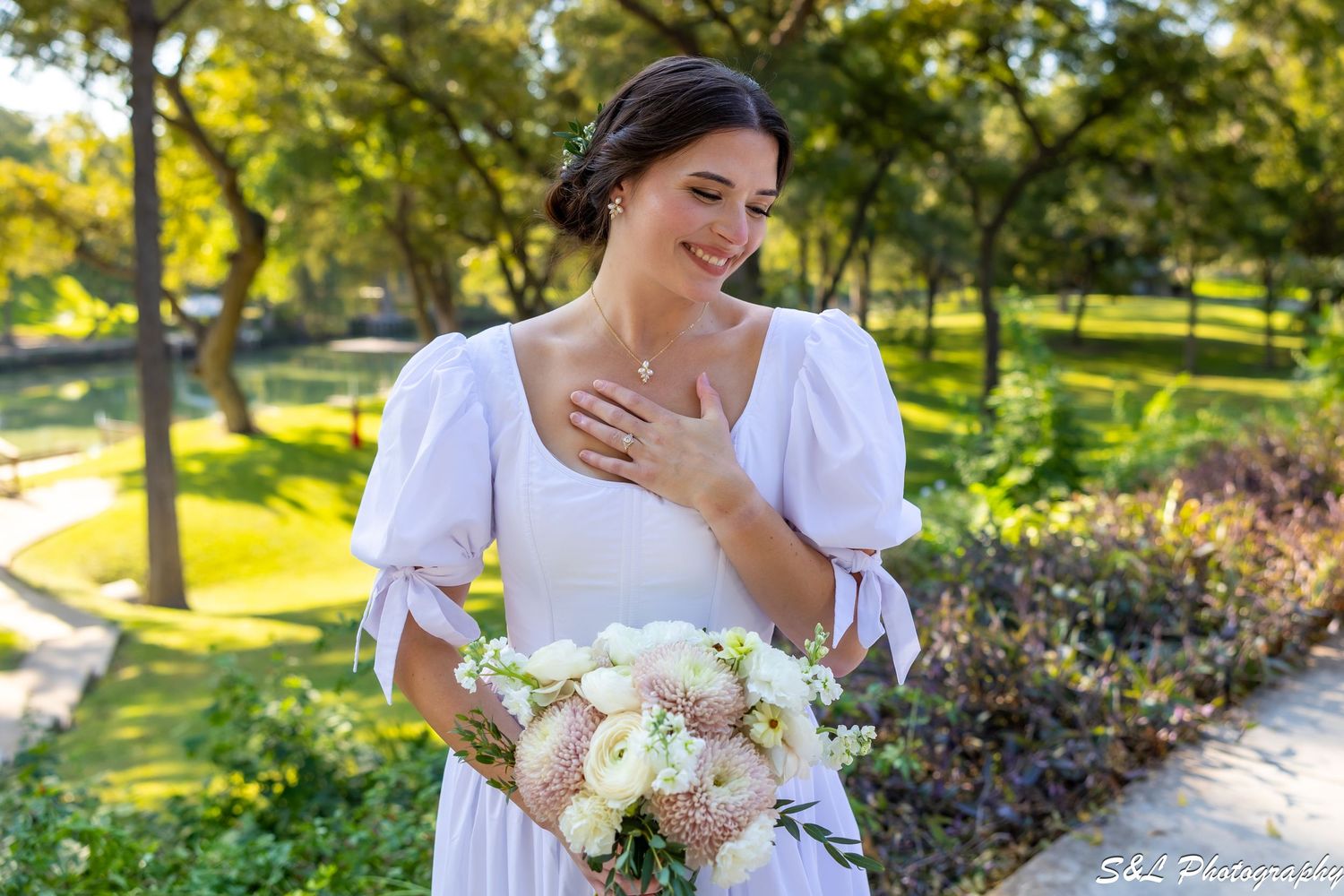 Person in white dress holding bouquet laughs joyfully in a sunny garden setting.