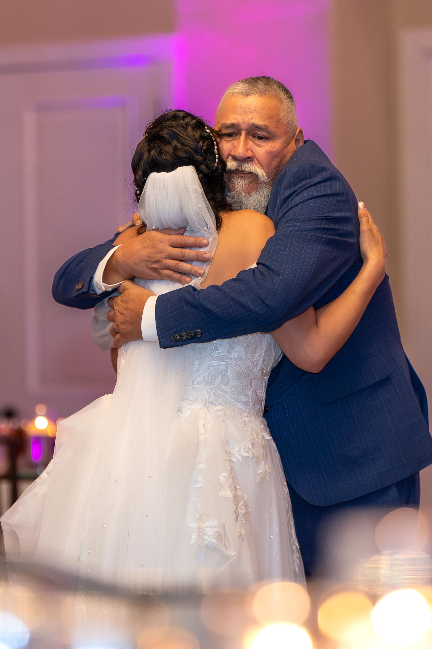 Couple shares romantic dance moment in elegant ballroom with purple lighting.