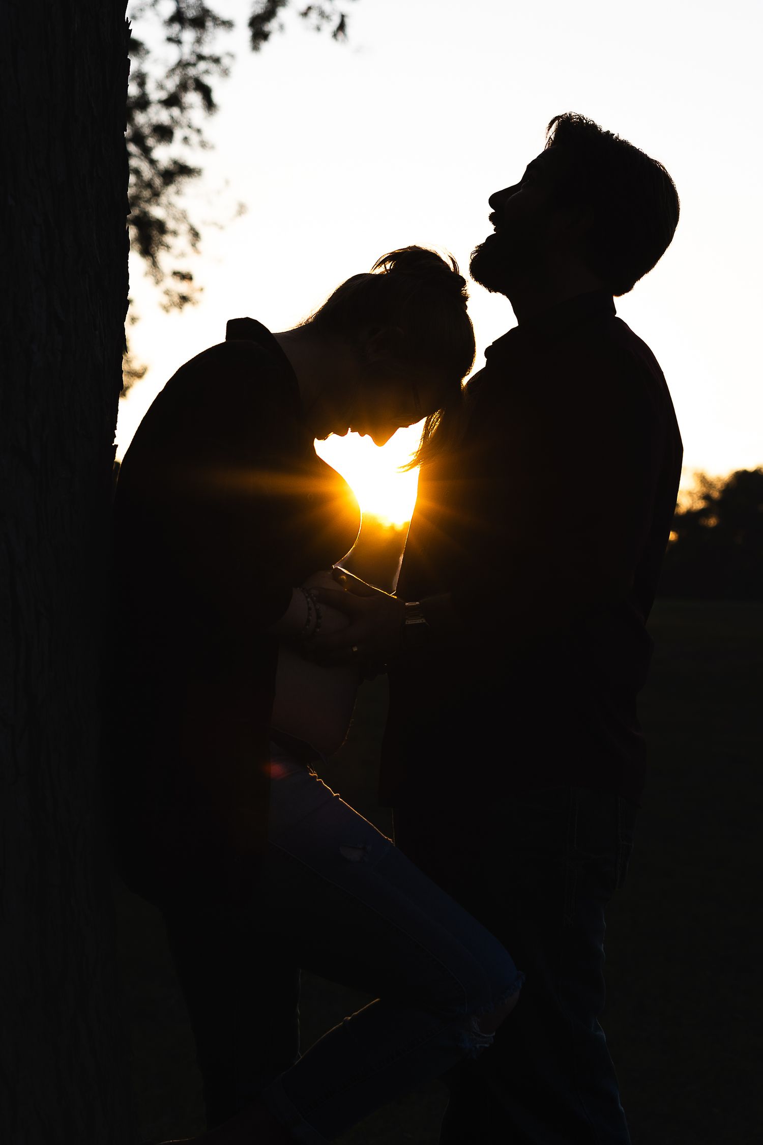 Silhouette of a couple against sunset with sun rays peeking through creating a romantic backlit effect.