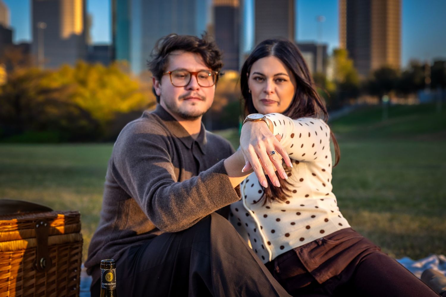 Couple relaxing on blanket at sunset with downtown skyline in background.