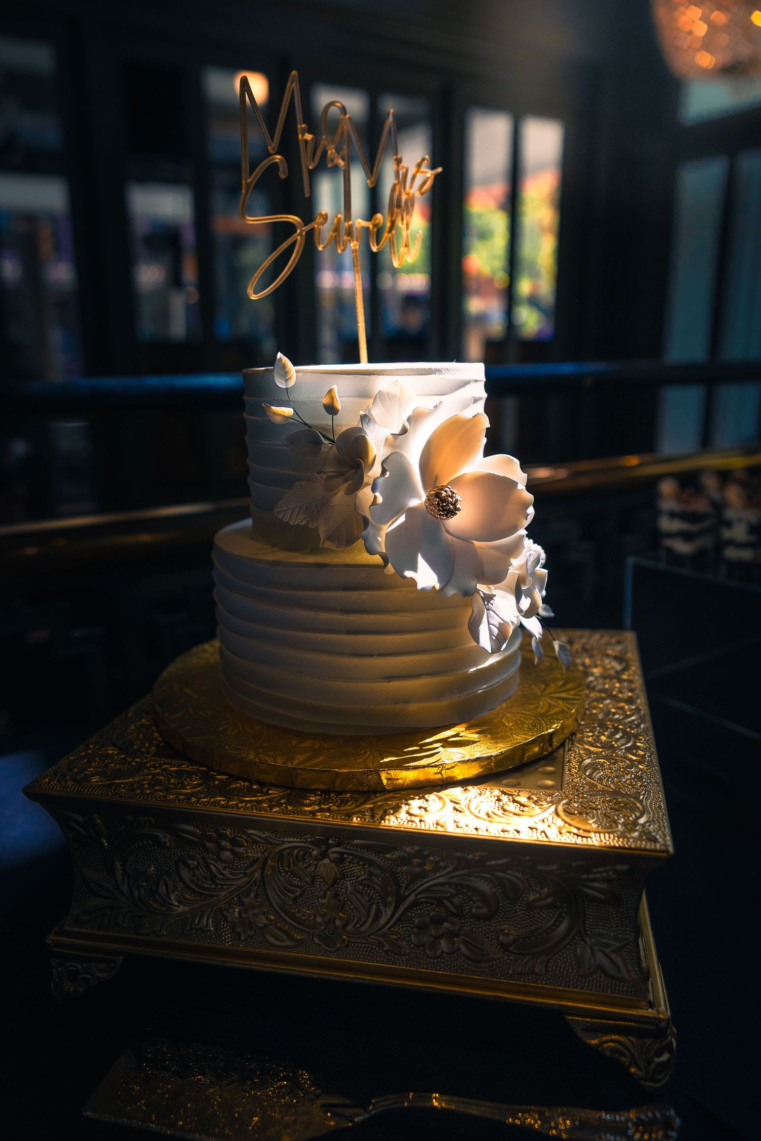 Elegant white wedding cake with butterfly decorations and gold topper on ornate stand.