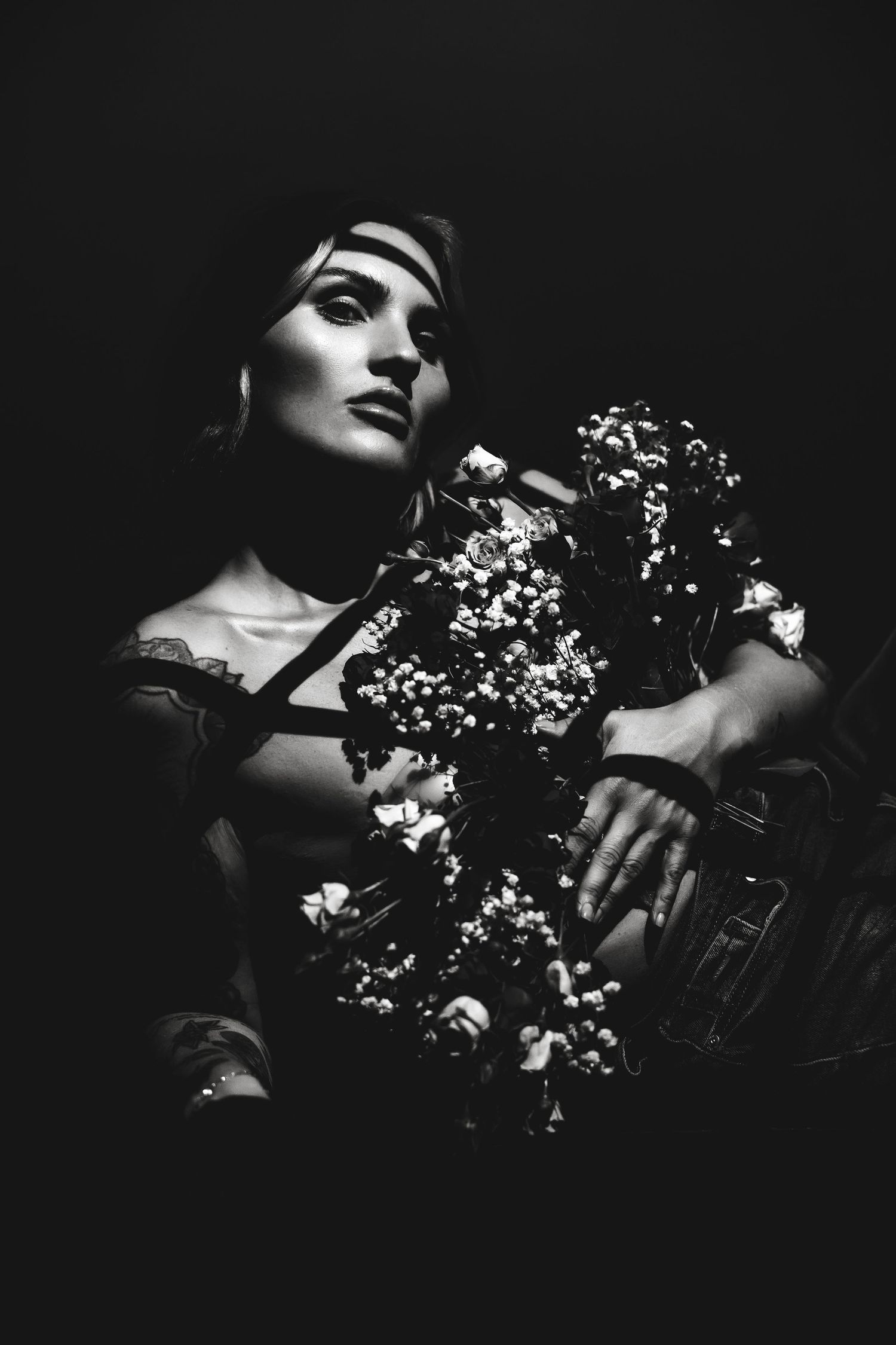Dramatic black and white portrait with flowers creating artistic shadows.