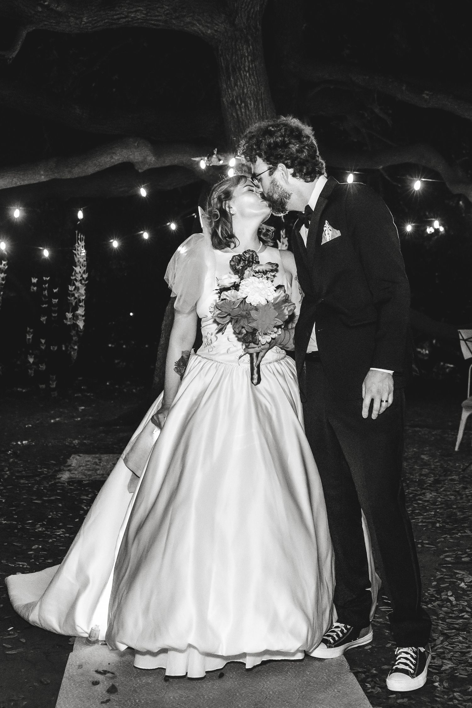 Black and white photo of romantic moment under string lights at outdoor wedding reception.