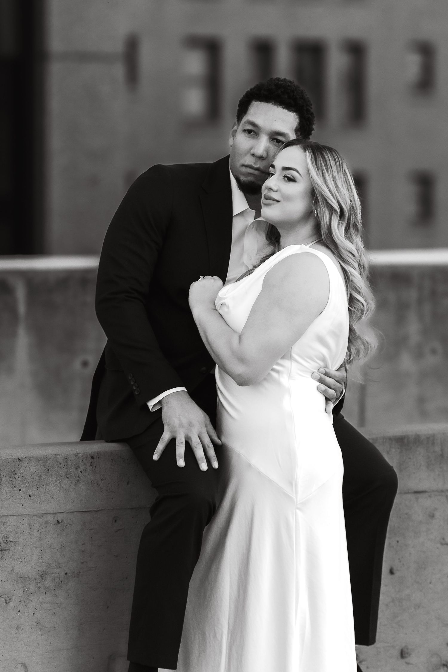 Black and white portrait of couple sharing intimate moment against concrete wall.