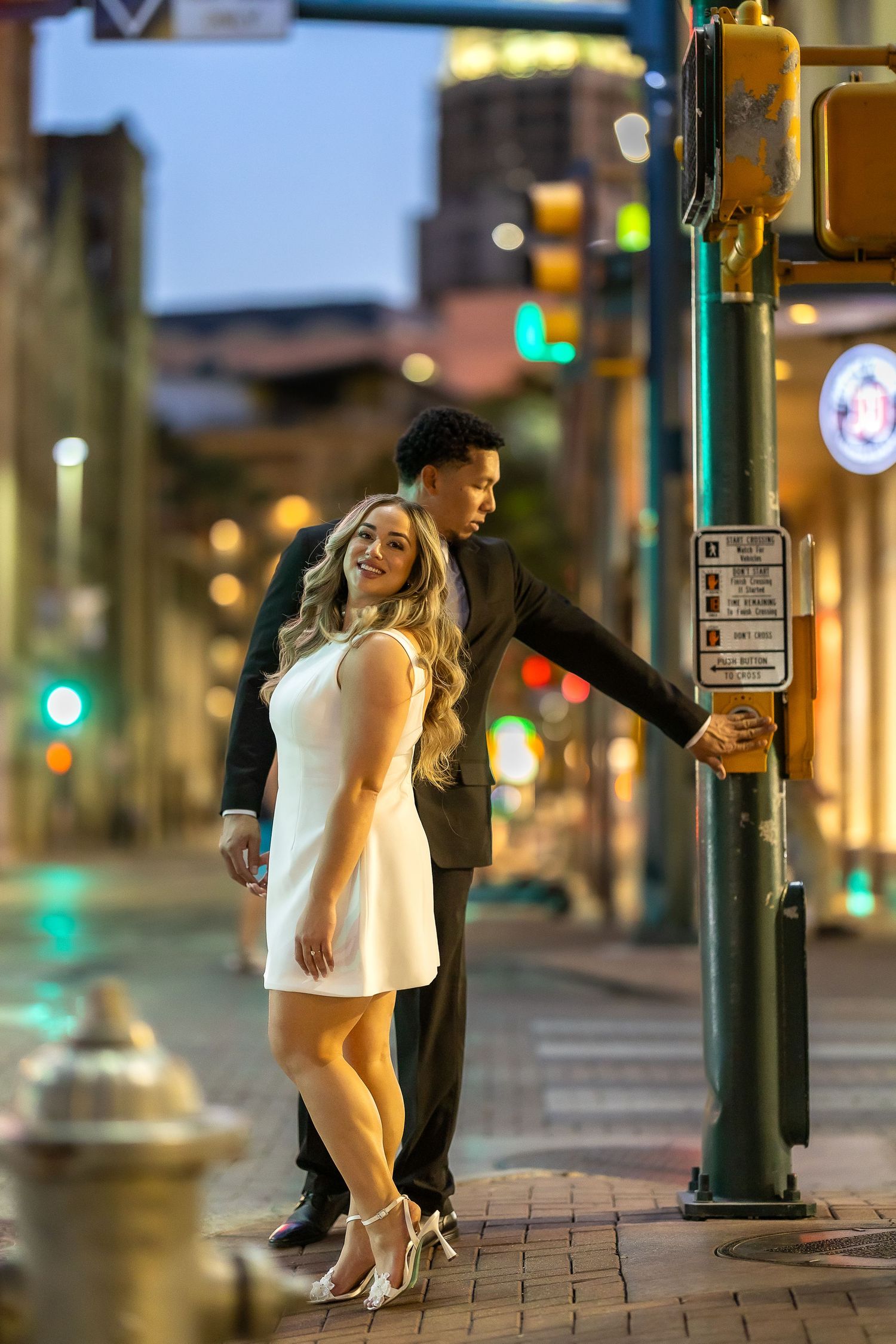 Playful couple poses near traffic light pole on urban street at dusk.