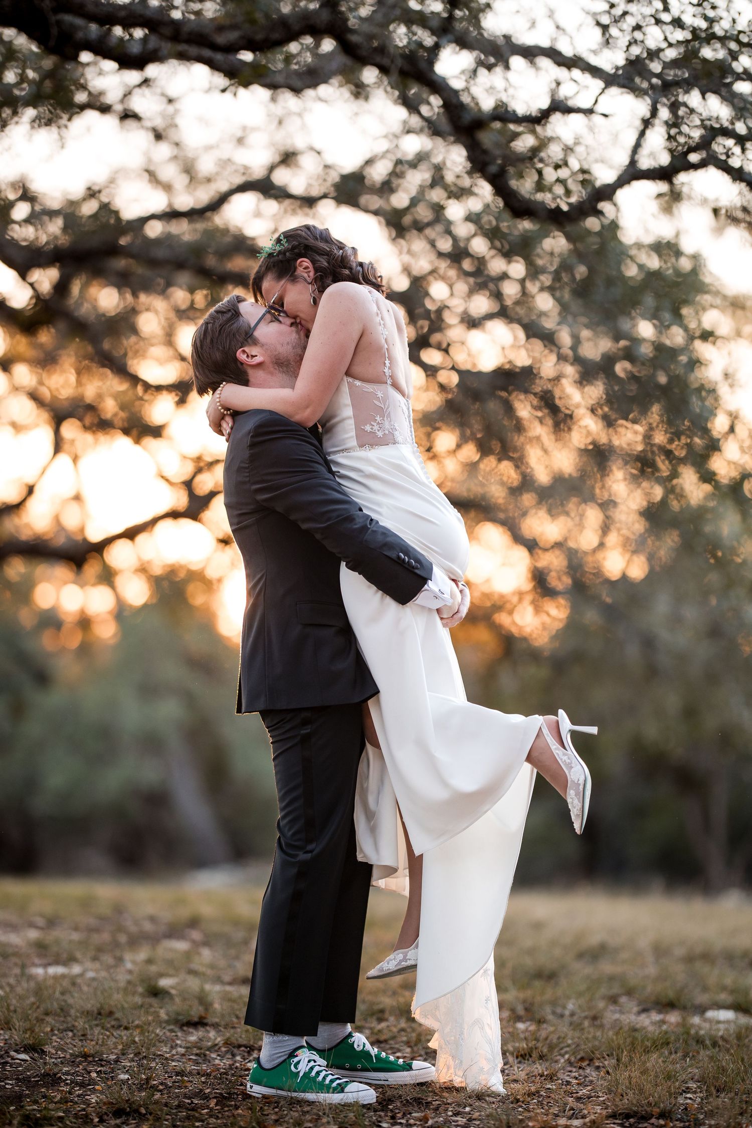 Couple in formal wear share playful moment at sunset with groom wearing green sneakers.