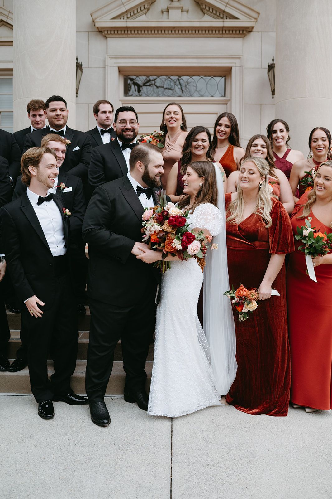 Wedding party in formal attire with bridesmaids in burgundy dresses and groomsmen in black tuxedos pose together at the Robert Carr Chapel.