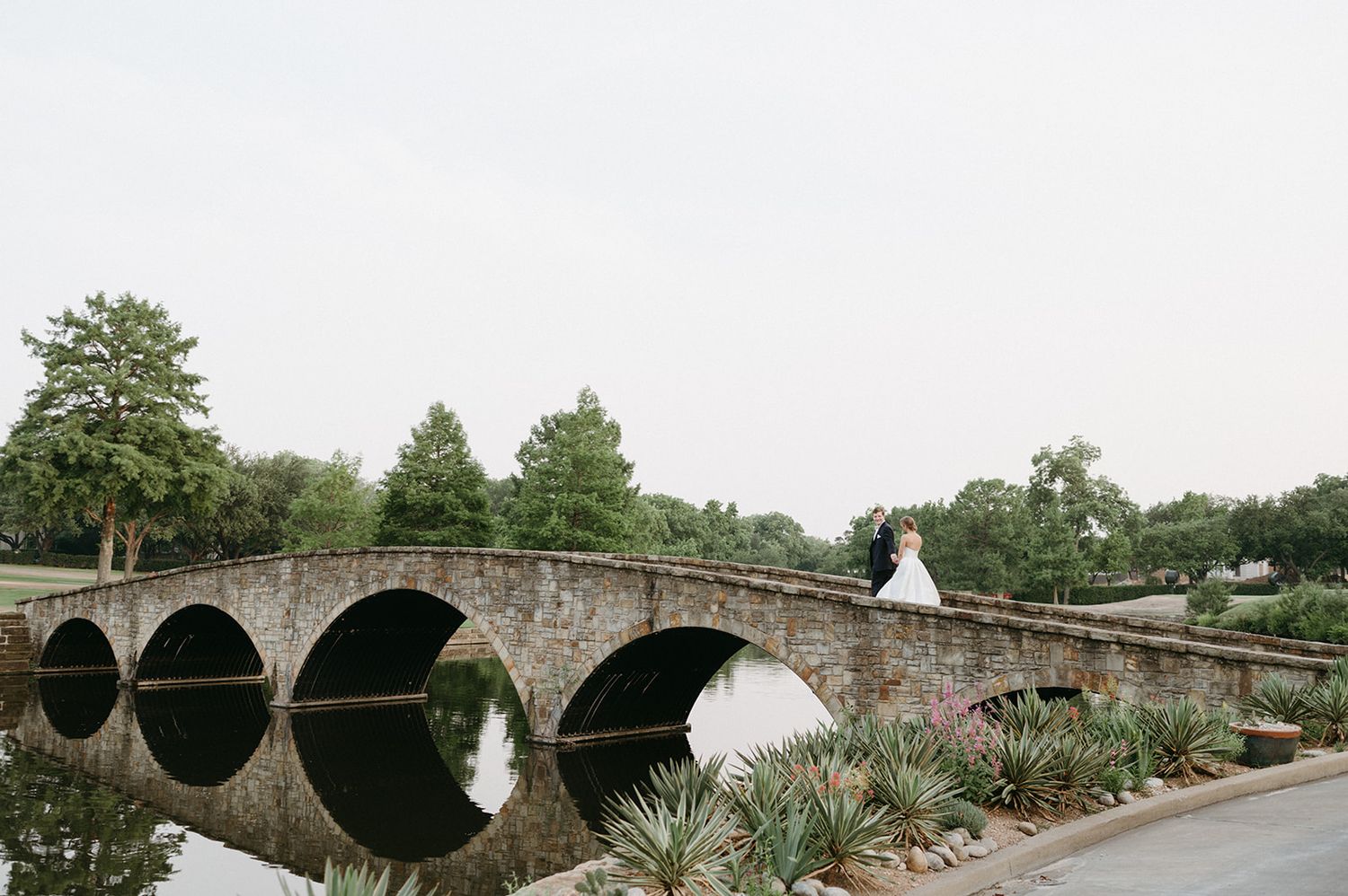 A historic stone bridge with multiple arches spans across a river in a scenic countryside setting at the Highland Park Country Club.