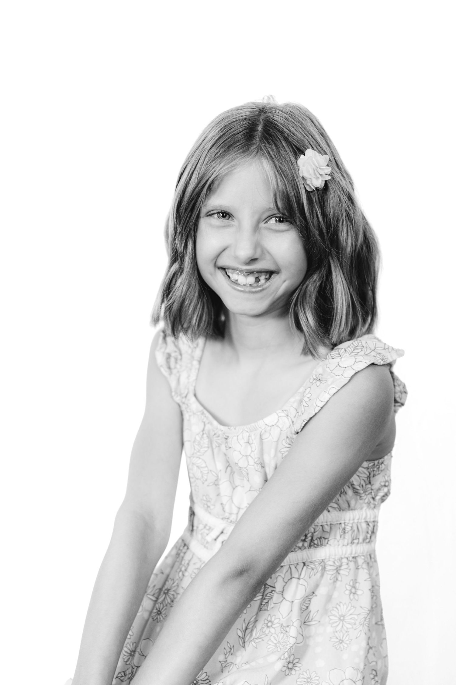 Black and white portrait of a smiling young girl with a flower hair clip wearing a sleeveless dress.