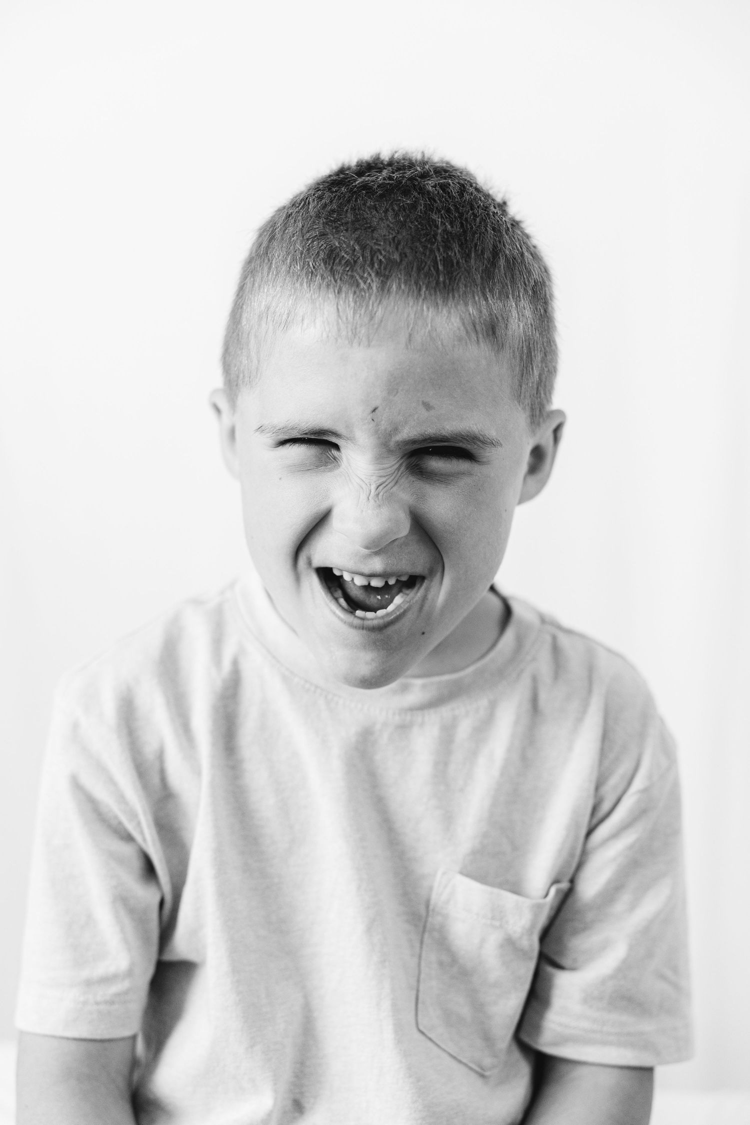 Black and white portrait of a laughing young boy in a t-shirt, eyes squinted with joy.