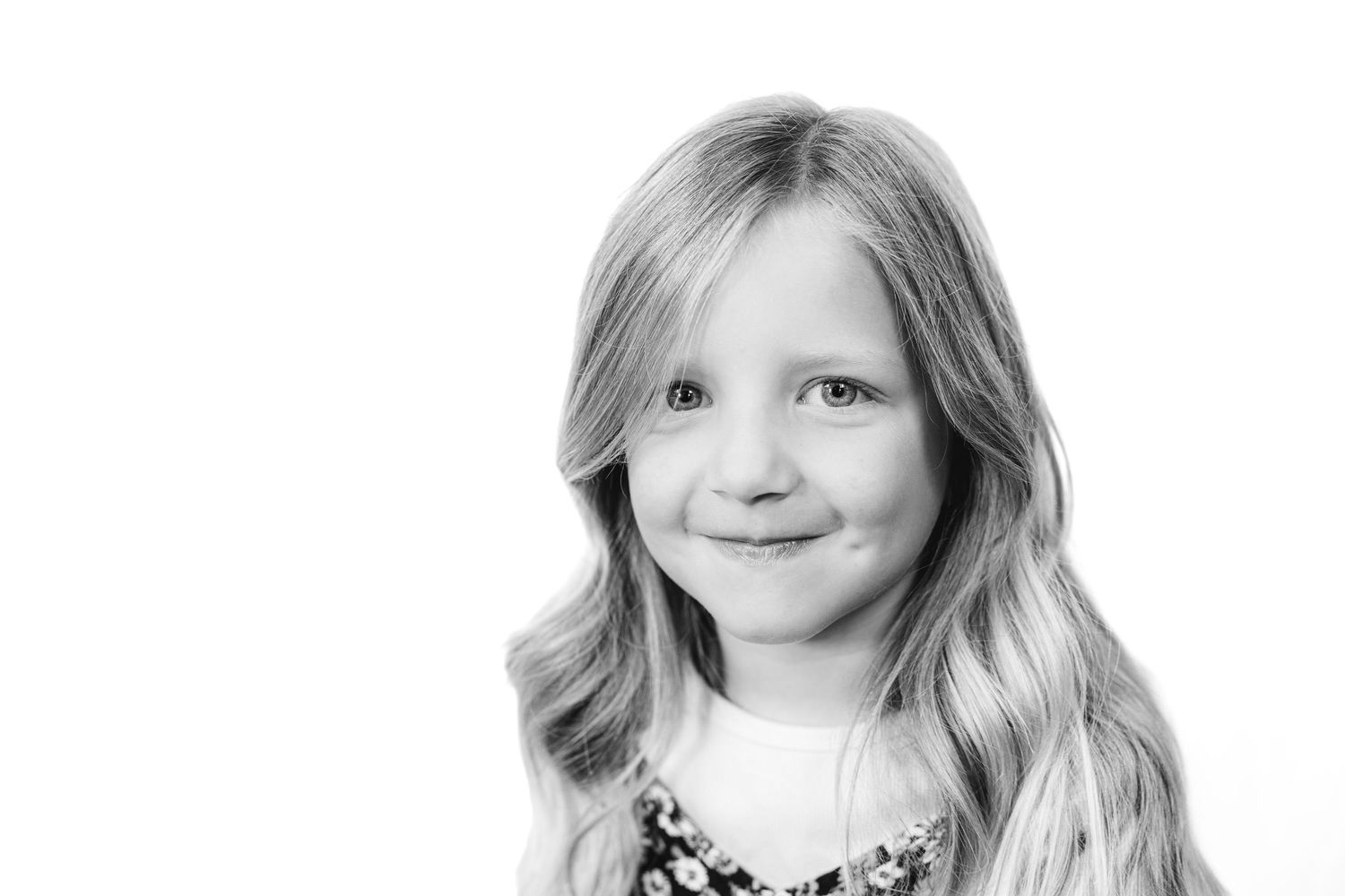 Black and white close-up portrait of a young blonde girl with long wavy hair smiling softly.