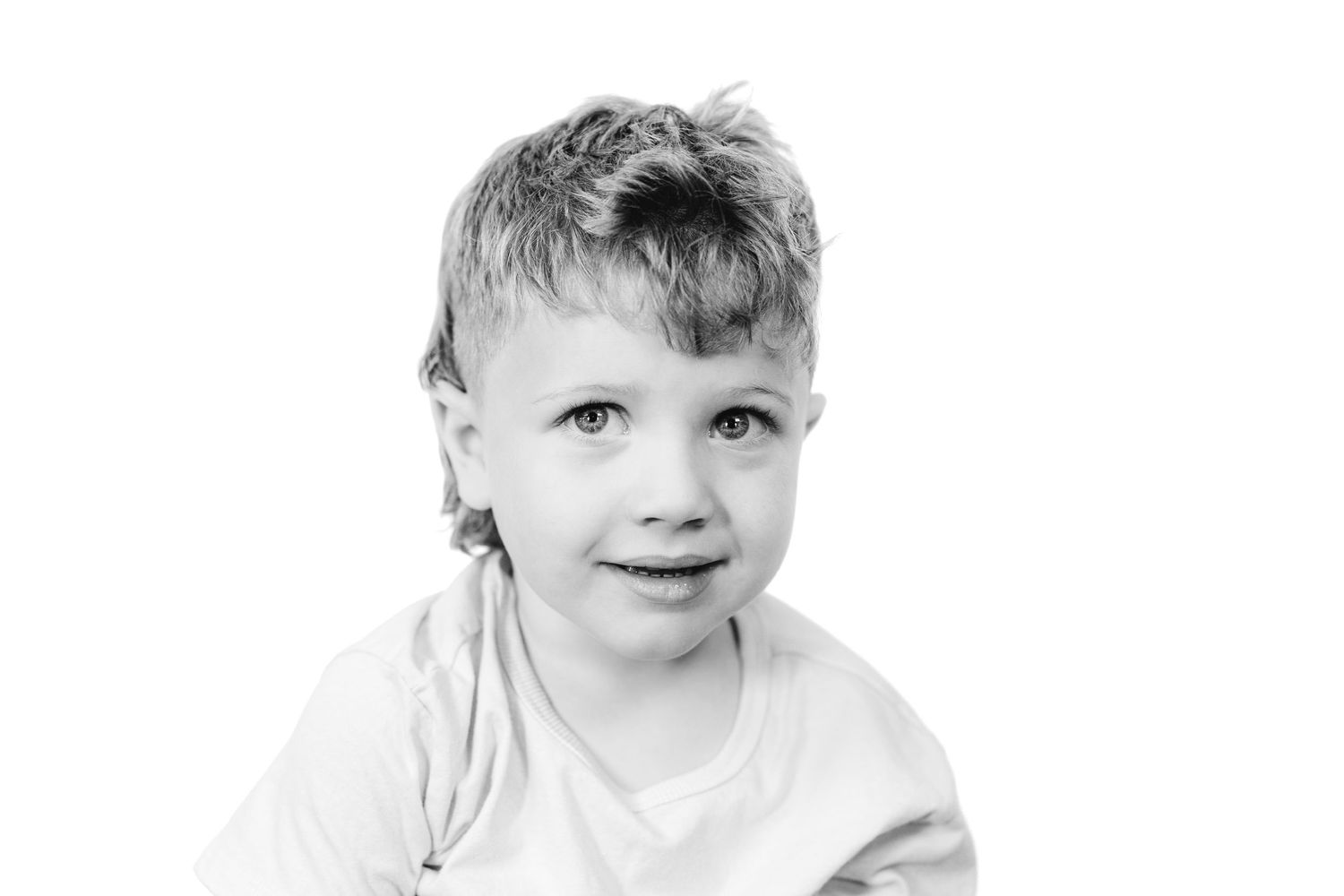 Black and white portrait of a young smiling boy with tousled hair wearing a white t-shirt.