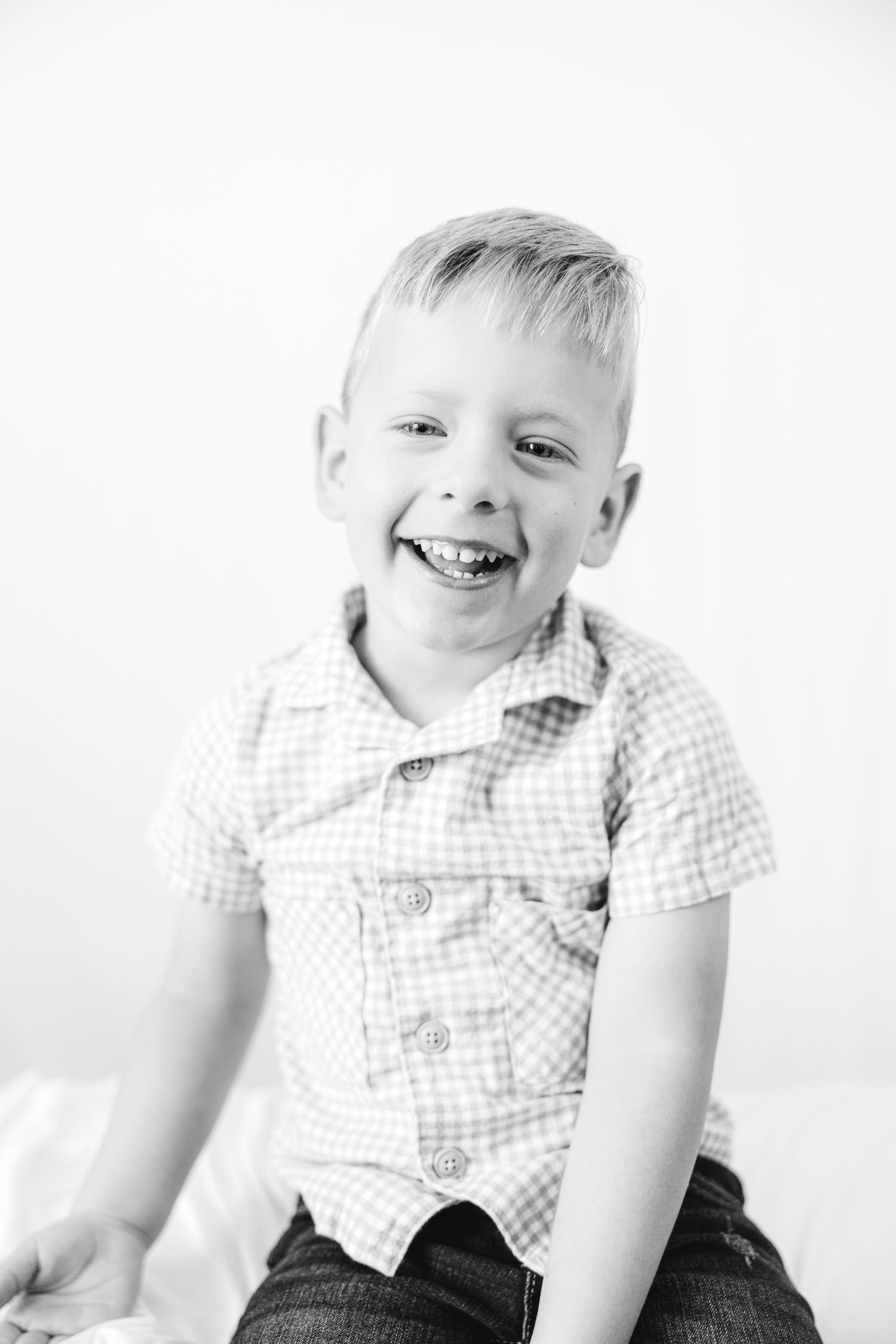 Black and white portrait of a happy young blonde boy laughing in a checkered shirt.