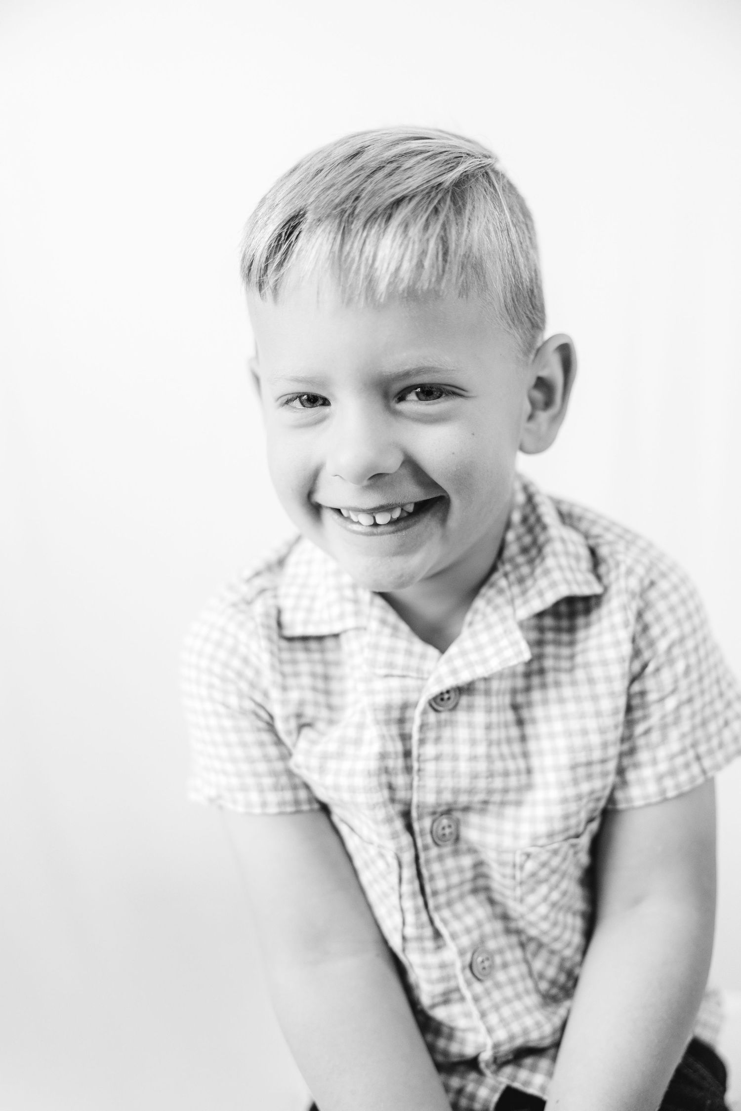 Black and white portrait of a smiling young boy in a plaid shirt posing against a white background.