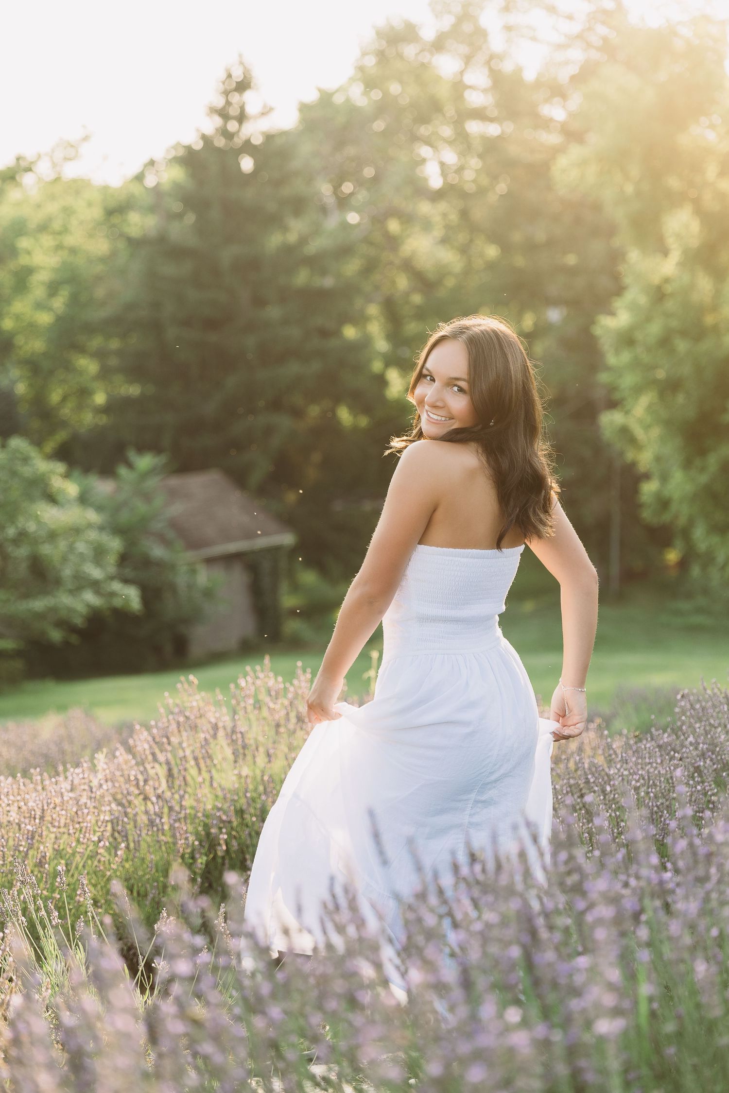 Young woman in white strapless dress smiling in lavender field at golden hour sunset. Katie Chamberlain Photography
