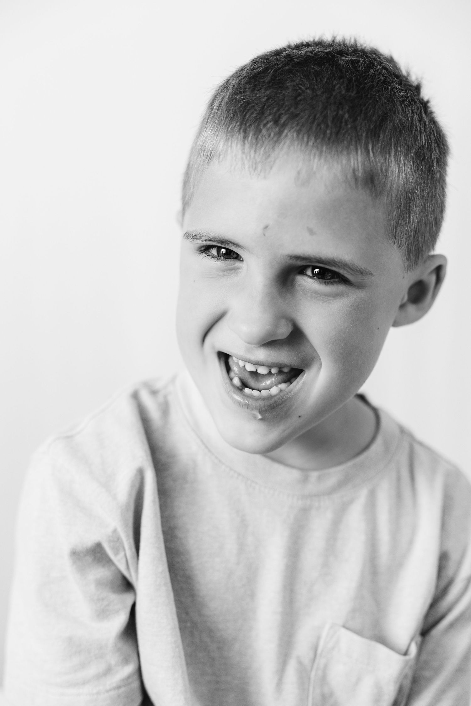 Black and white portrait of a smiling young boy with short hair wearing a t-shirt with chest pocket.