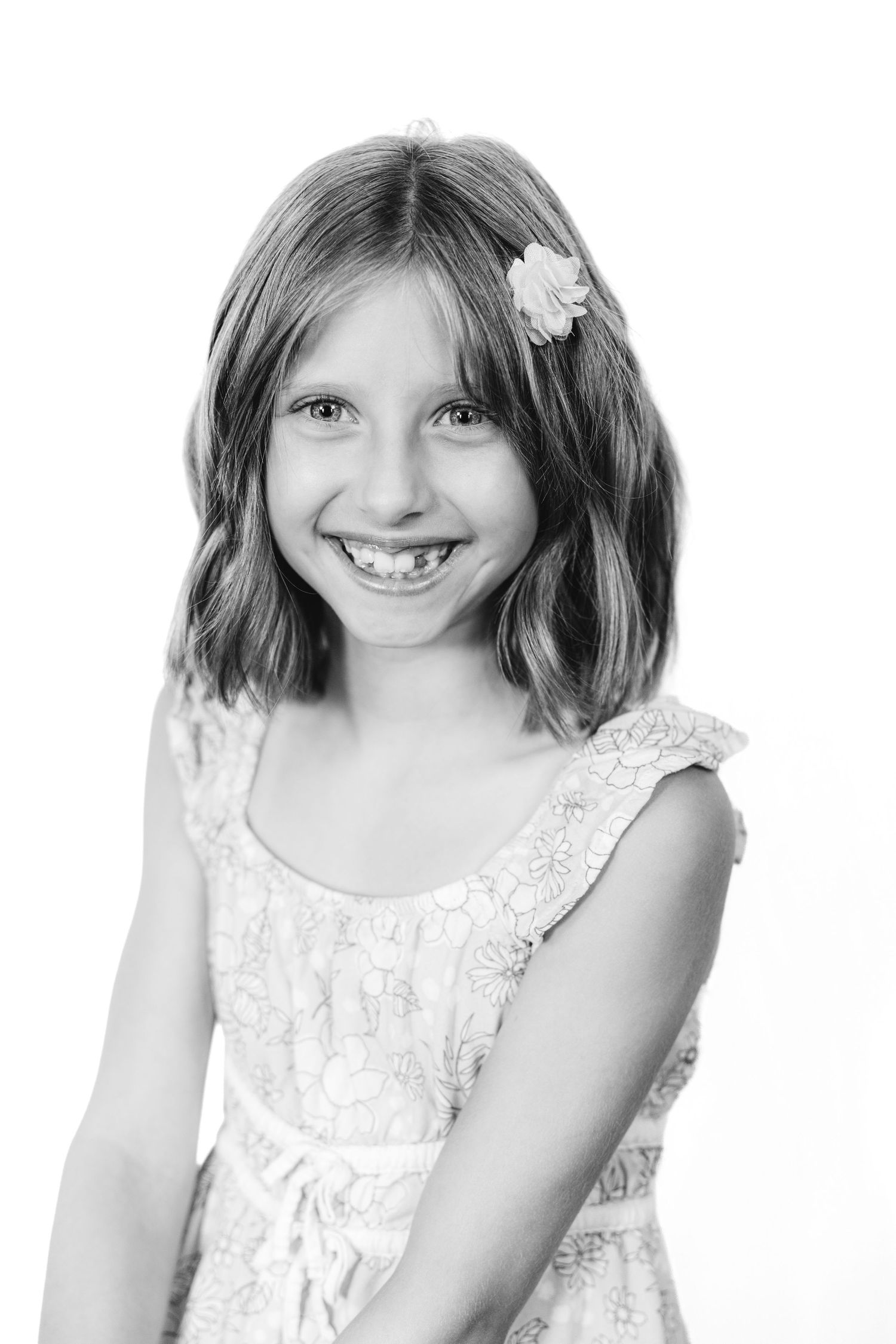 Black and white portrait of a smiling young girl with a flower hair clip wearing a lace dress.