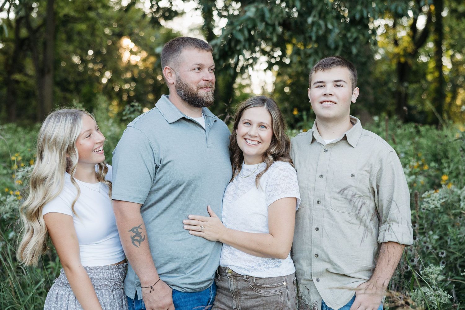A happy family of four poses outdoors among lush greenery for a professional portrait photo.