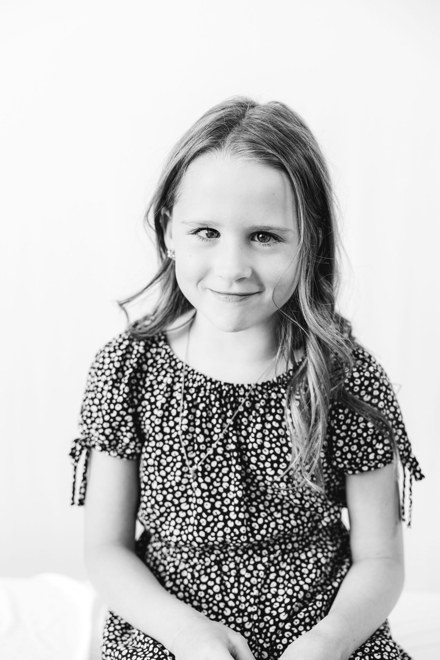 Black and white portrait of a young girl with long hair wearing a floral dress, smiling softly at the camera.