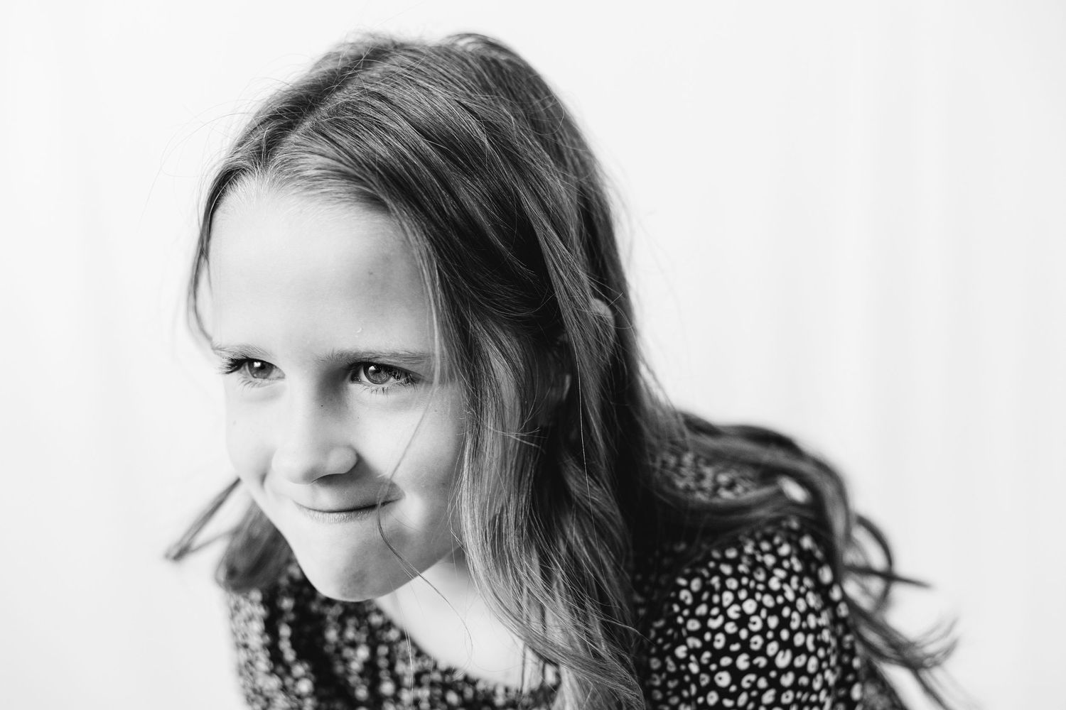 Black and white portrait of a smiling young girl with long hair wearing a floral dress.