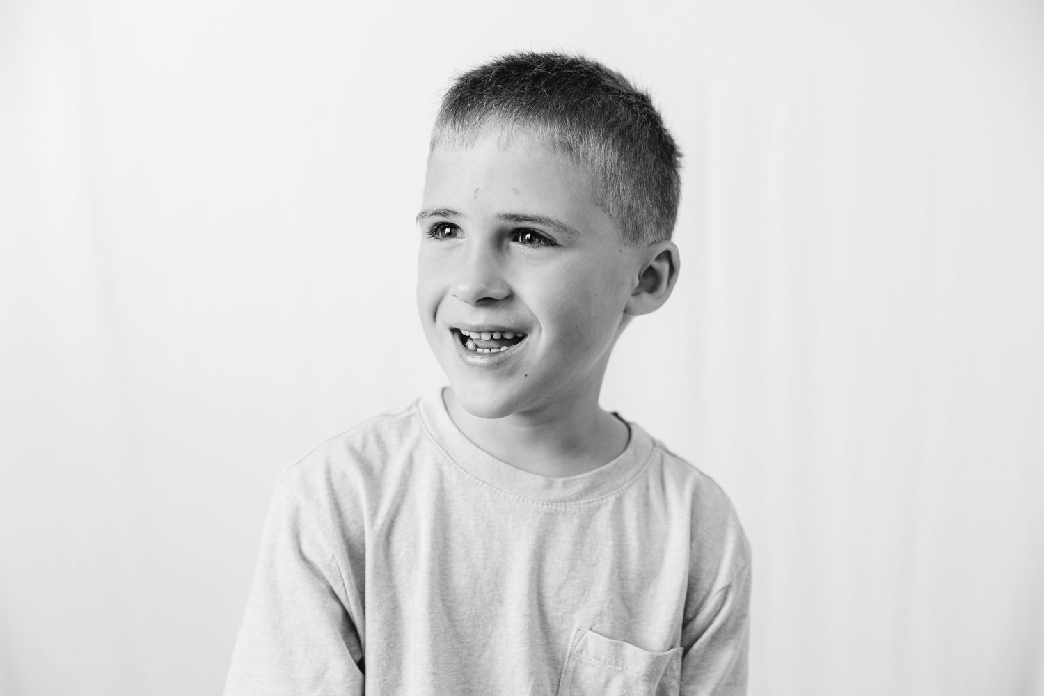 Black and white portrait of a smiling young boy with short hair wearing a t-shirt against a white background.