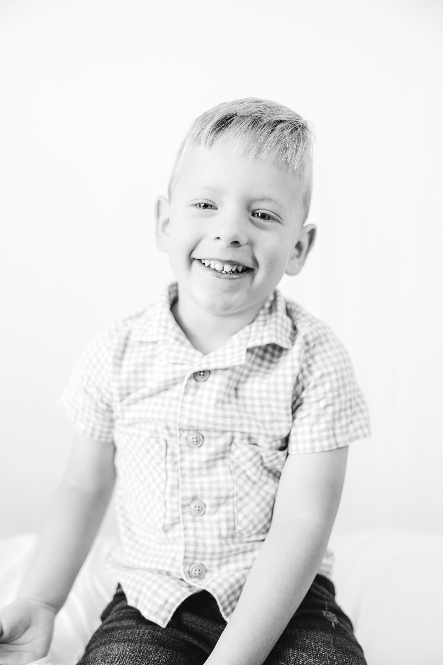 Black and white portrait of a happy young blonde boy laughing in a checkered shirt.