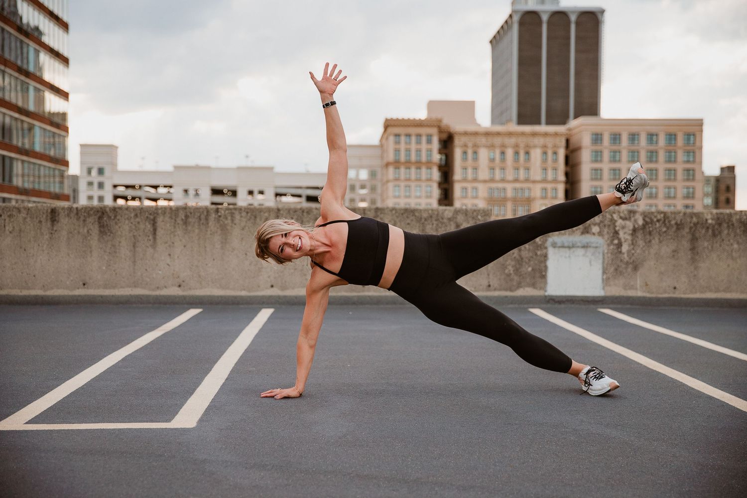 Woman performing a side plank exercise on a rooftop parking lot with city buildings in the background. Photographed by Katie Chamberlain