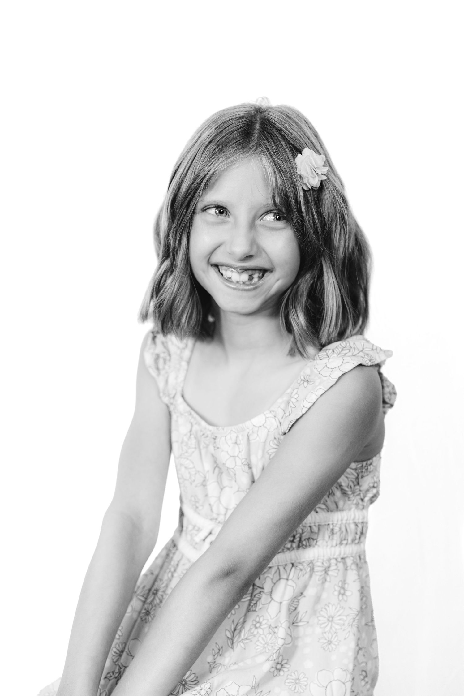 Black and white portrait of a smiling young girl with a flower hair clip wearing a lace dress.