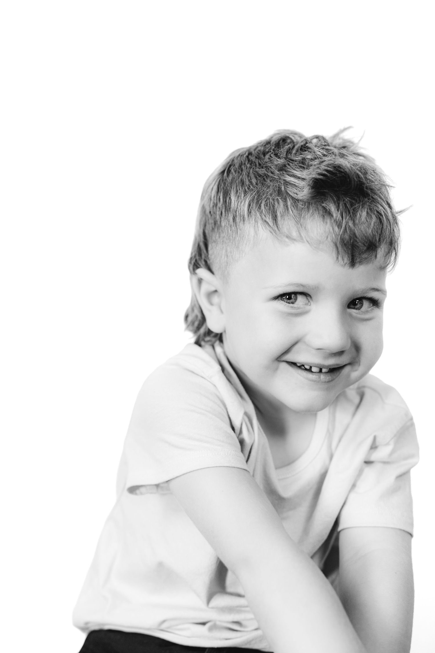 Black and white portrait of a smiling young boy in a white t-shirt posing against a white background.