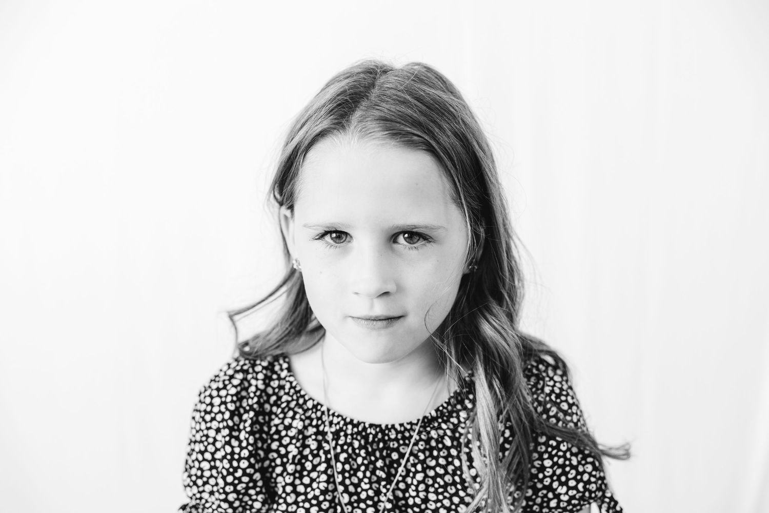 Black and white portrait of a young girl with long hair wearing a floral dress, looking seriously at the camera.