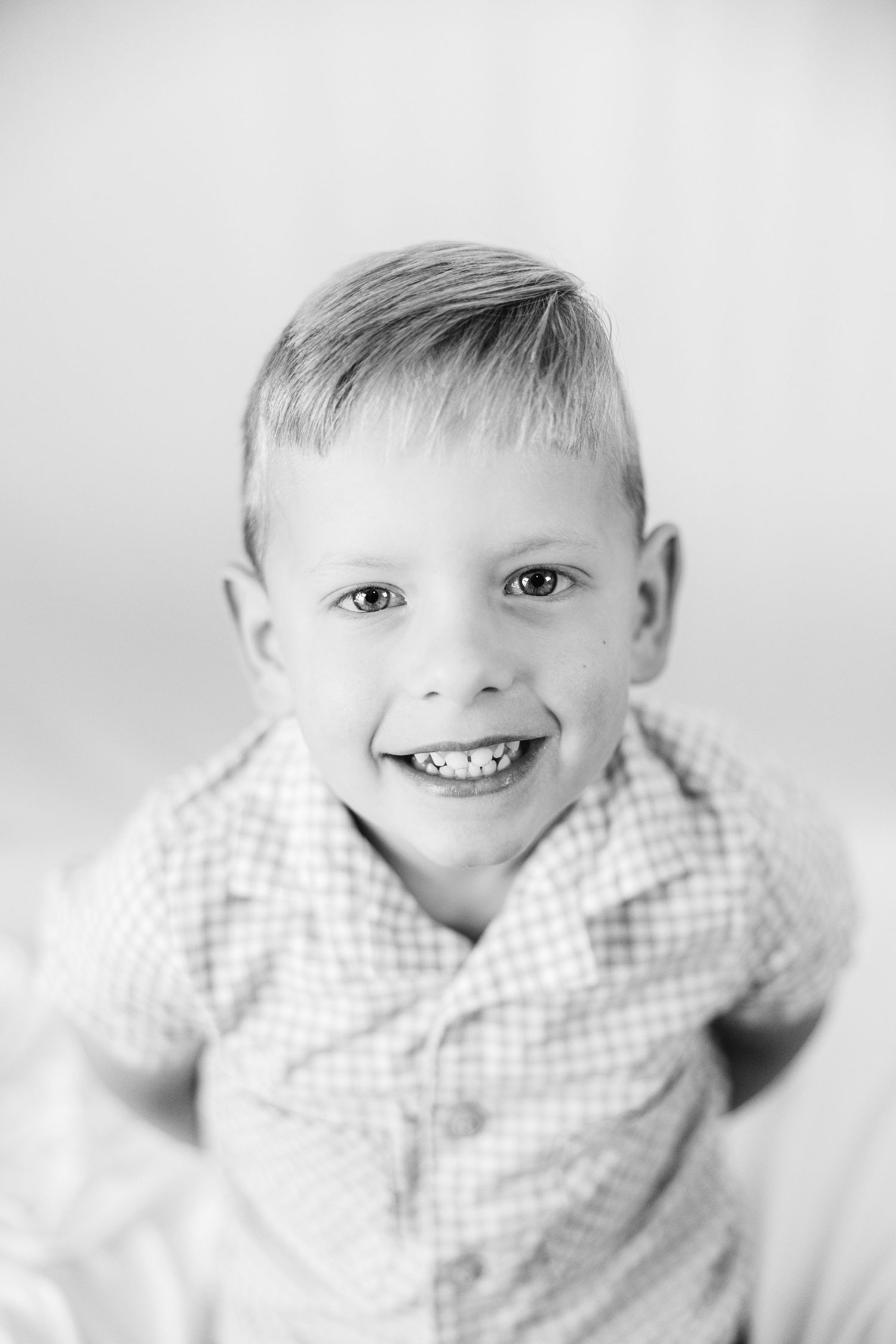 Black and white portrait of a smiling young boy with short hair wearing a checkered shirt.