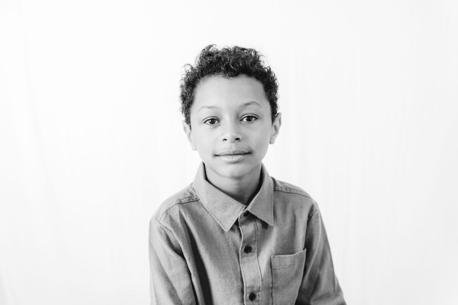 Black and white portrait of a young boy in a collared shirt smiling at the camera against a white background.