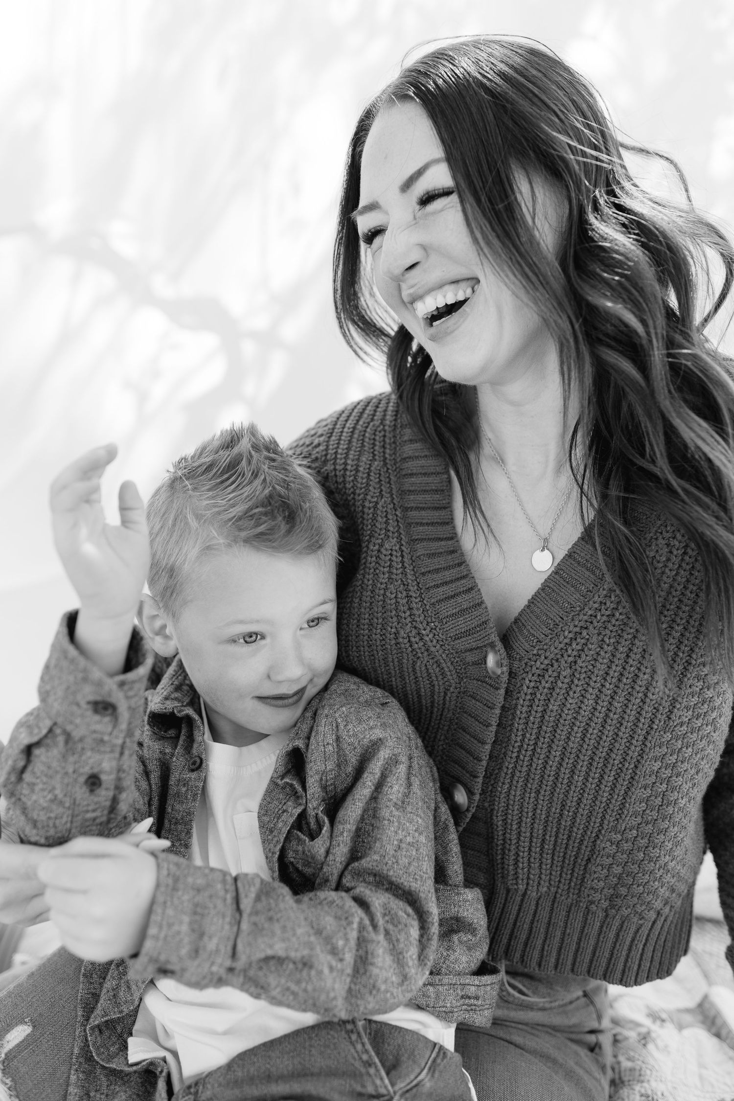 Black and white photo of a laughing mother and young son sitting together outdoors in winter.
