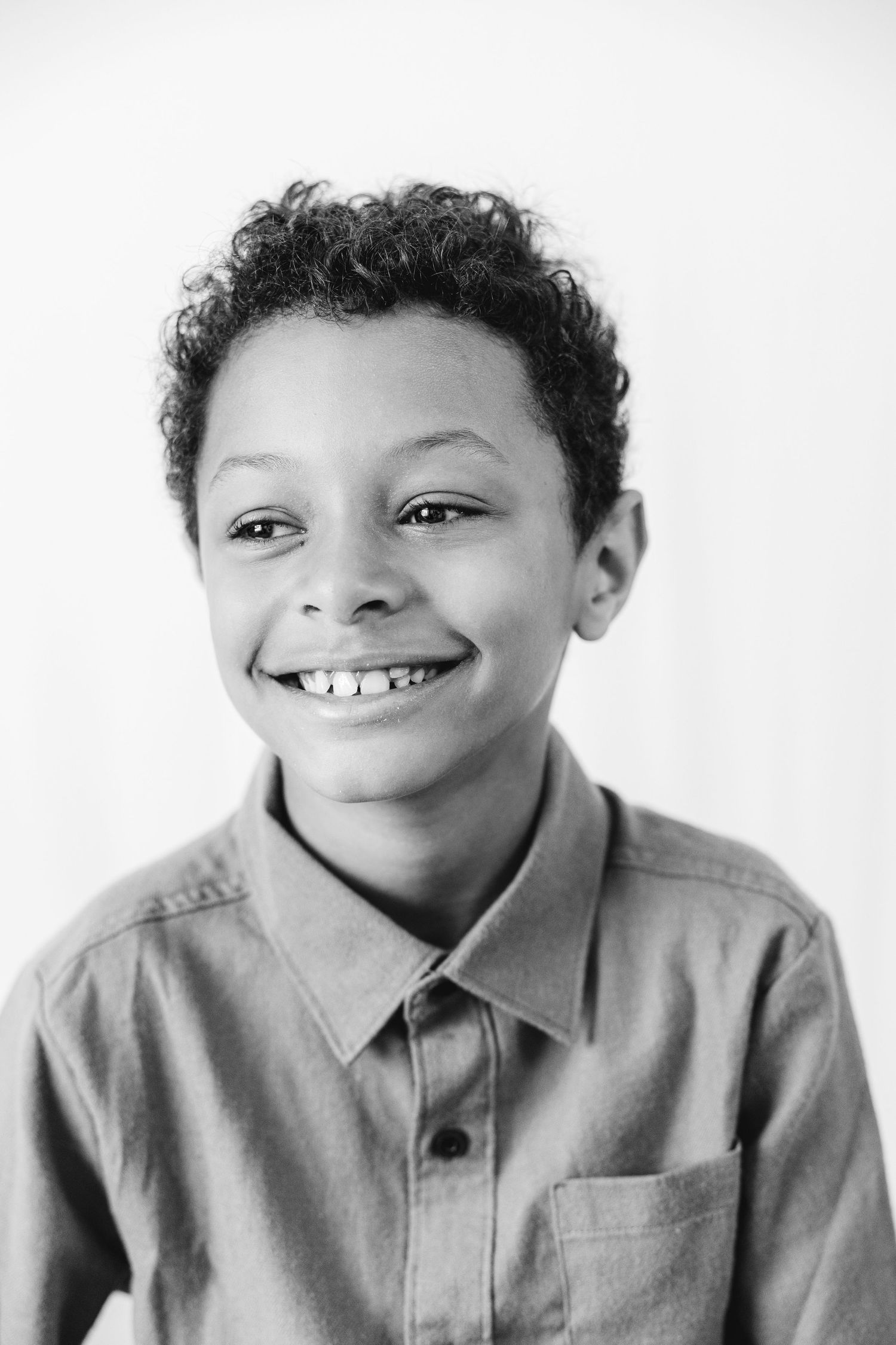 Black and white portrait of a smiling young boy with curly hair wearing a button-up shirt.