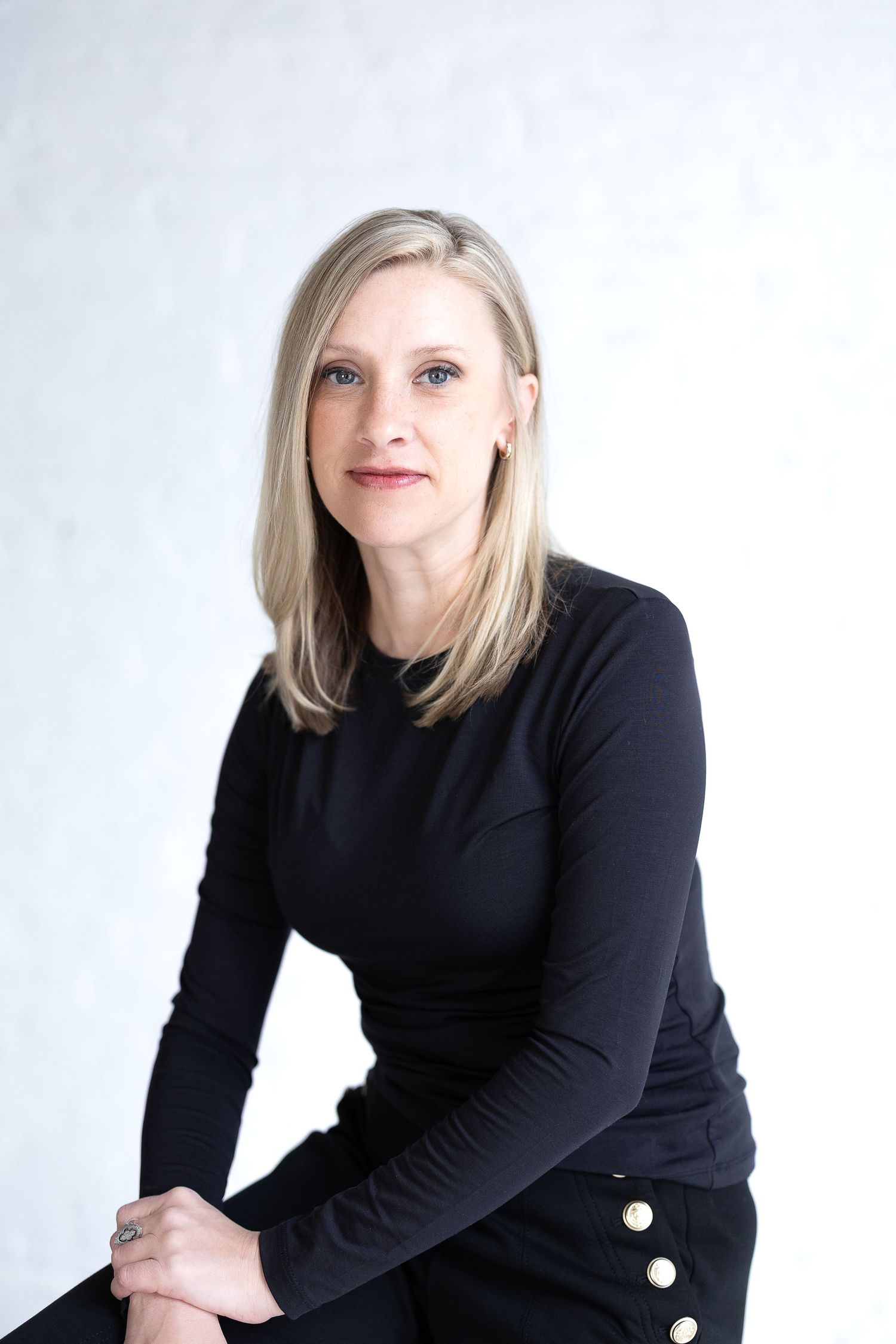 Professional headshot of a blonde woman in a black top against a light gray background. Katie Chamberlain Photography