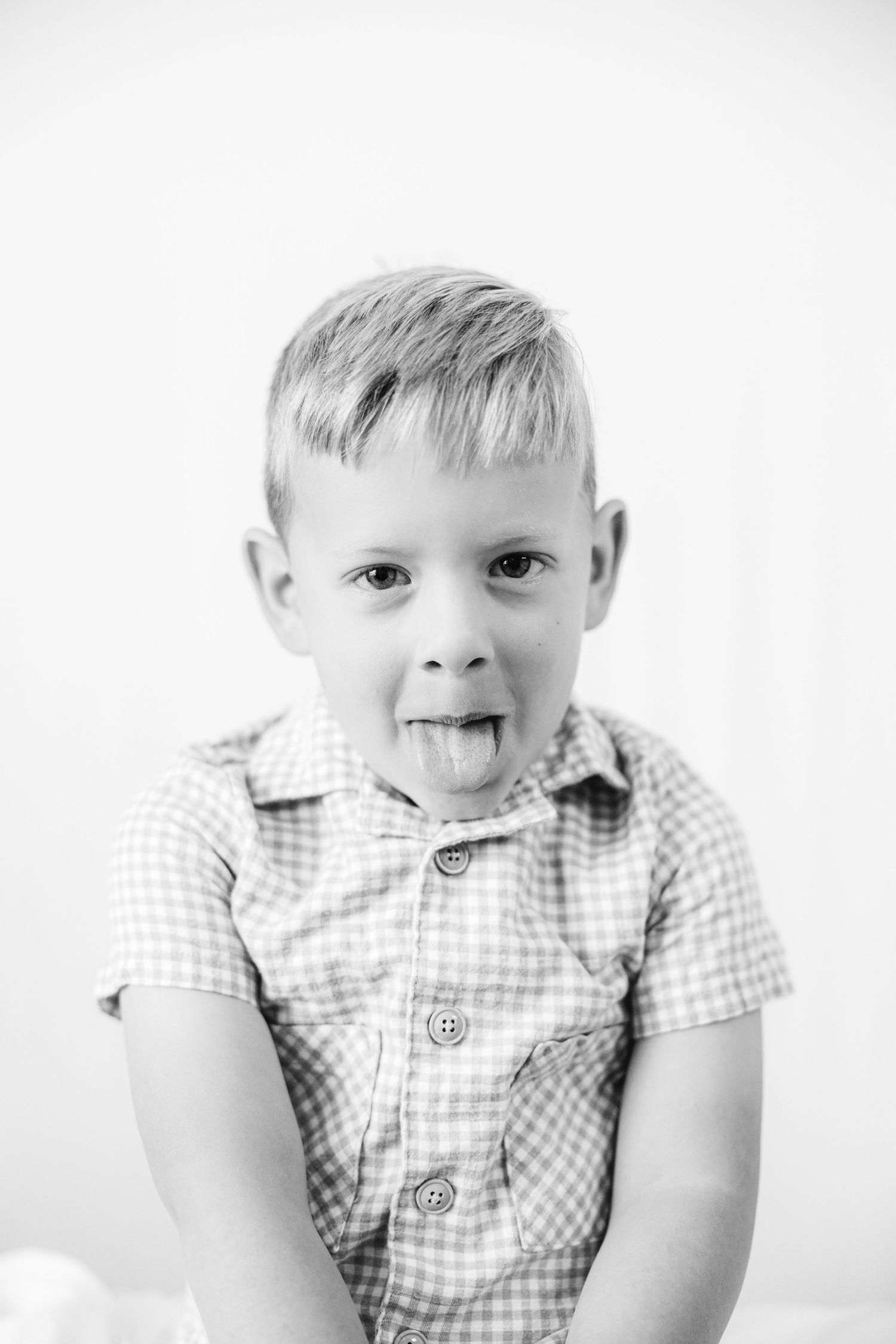 Black and white portrait of a young boy in a plaid shirt sticking his tongue out playfully.