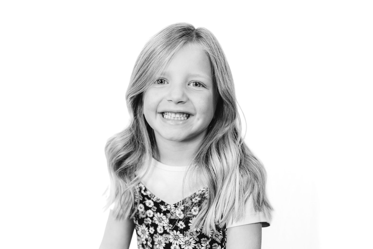 Black and white portrait of a smiling young blonde girl wearing a floral dress, studio photography.