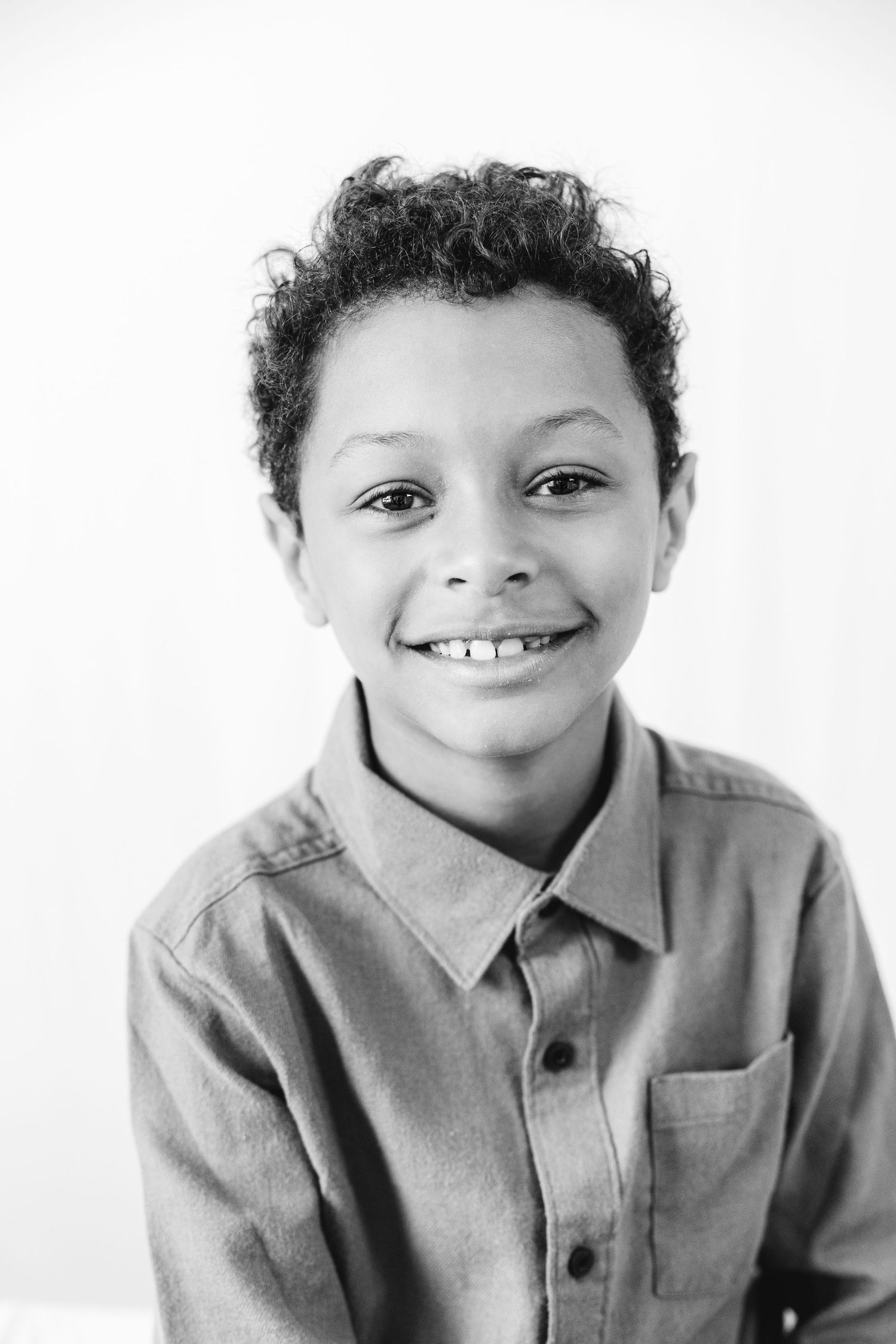 Black and white portrait of a smiling young boy with curly hair wearing a button-up shirt.