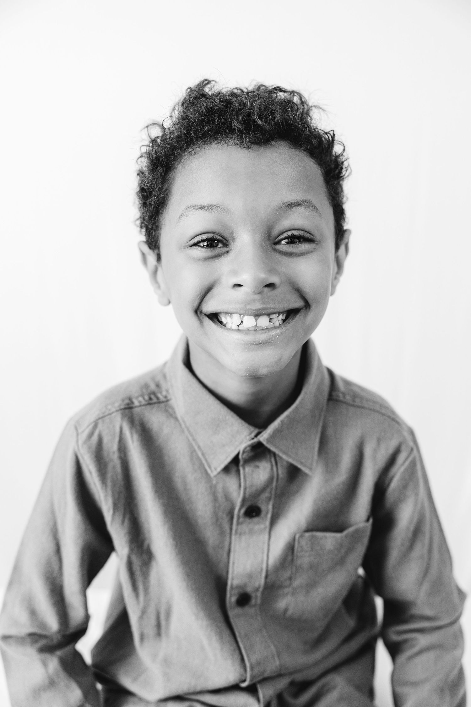 Black and white portrait of a smiling young boy with curly hair wearing a button-up shirt.