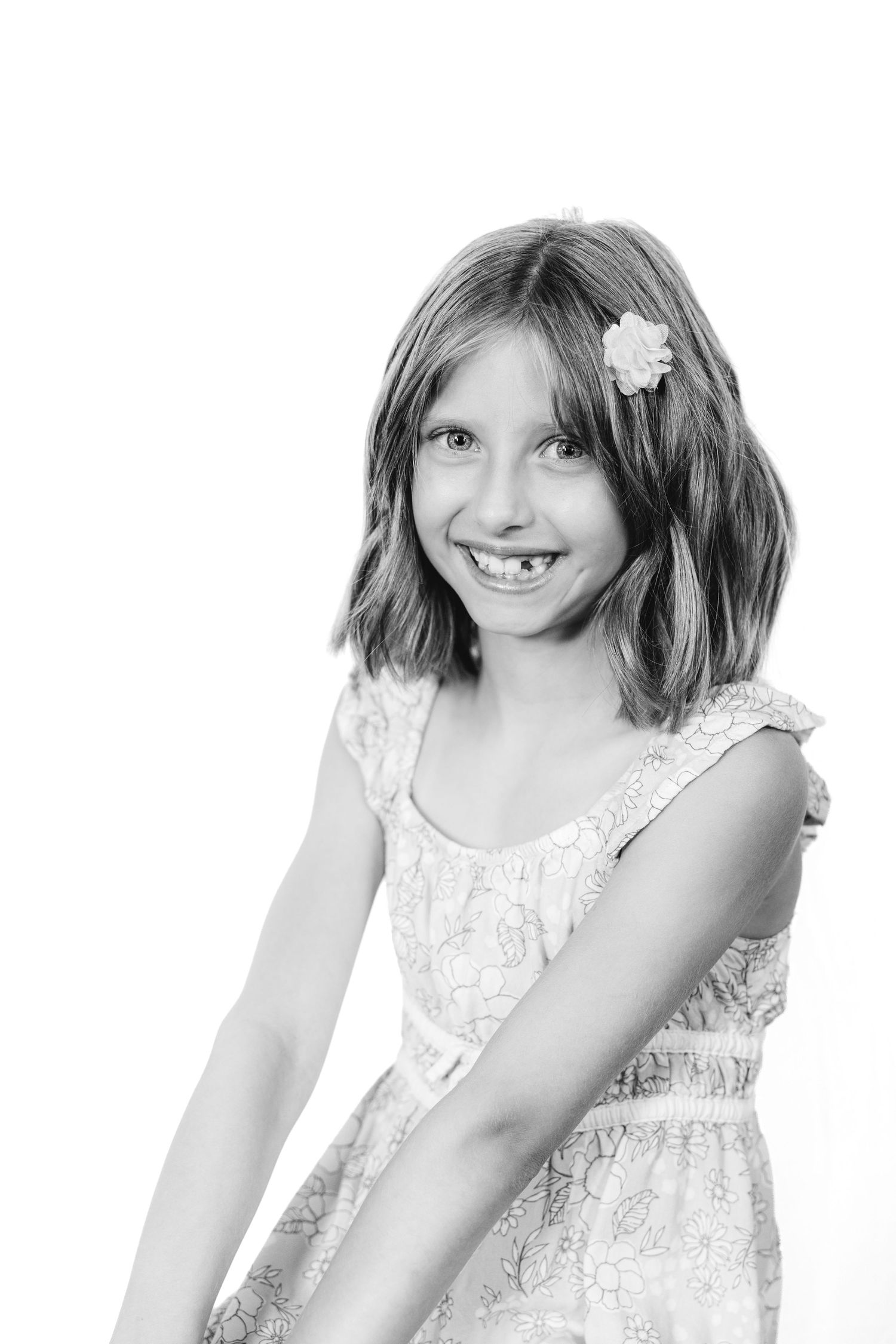 Black and white portrait of a smiling young girl with a flower in her hair wearing a lace dress.