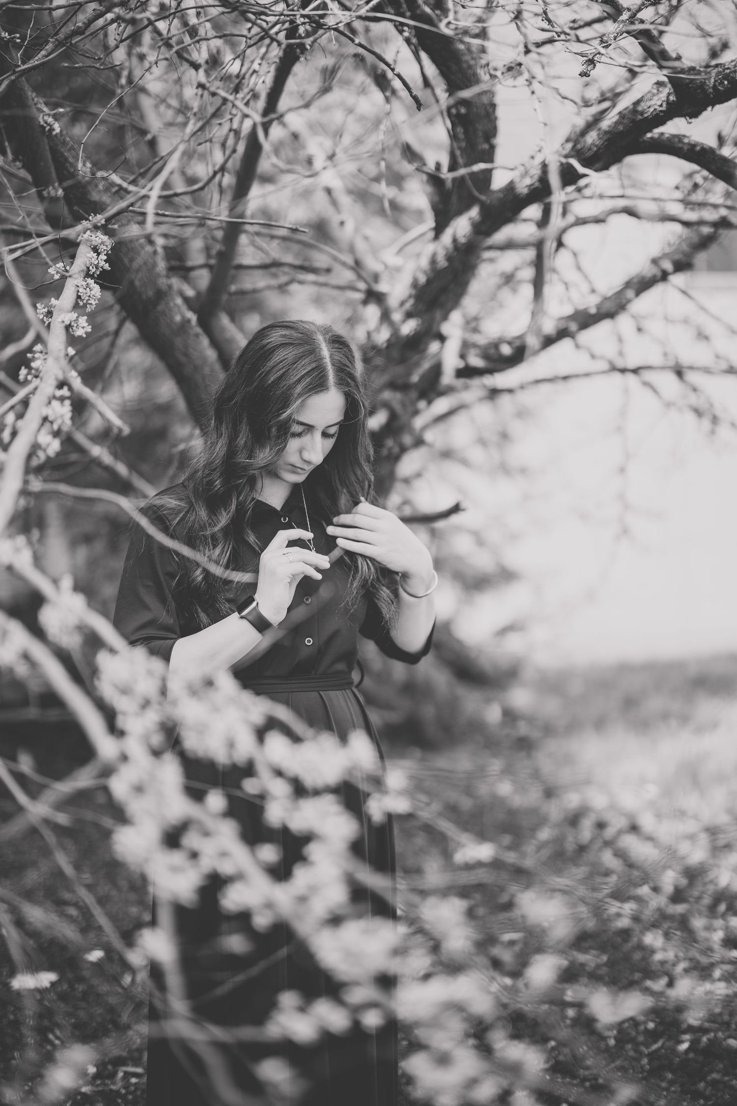 Black and white photo of a young woman standing among blooming spring trees, looking down Photographed by Katie Chamberlain Photography