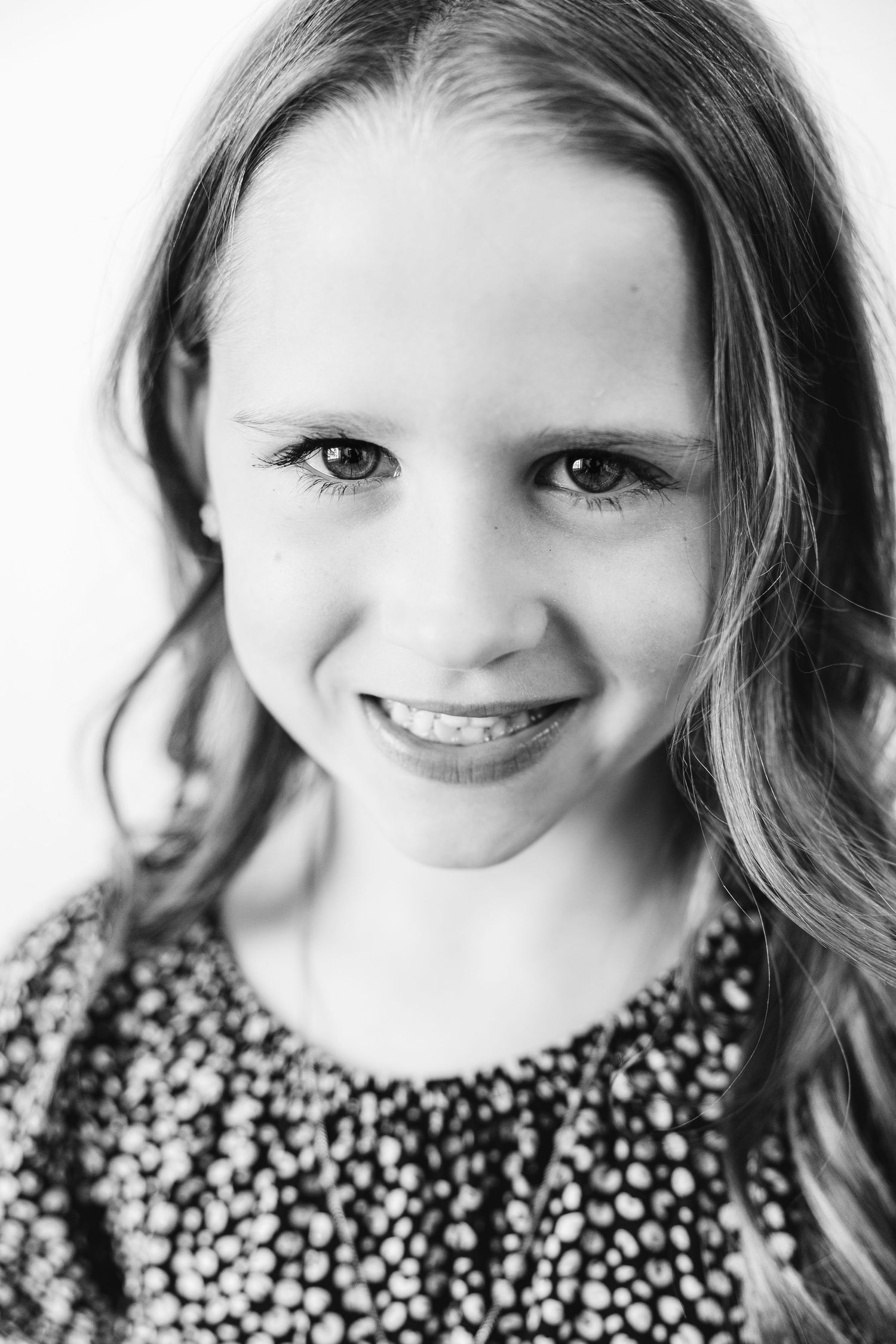 Black and white portrait of a smiling young girl with long hair wearing a patterned top.