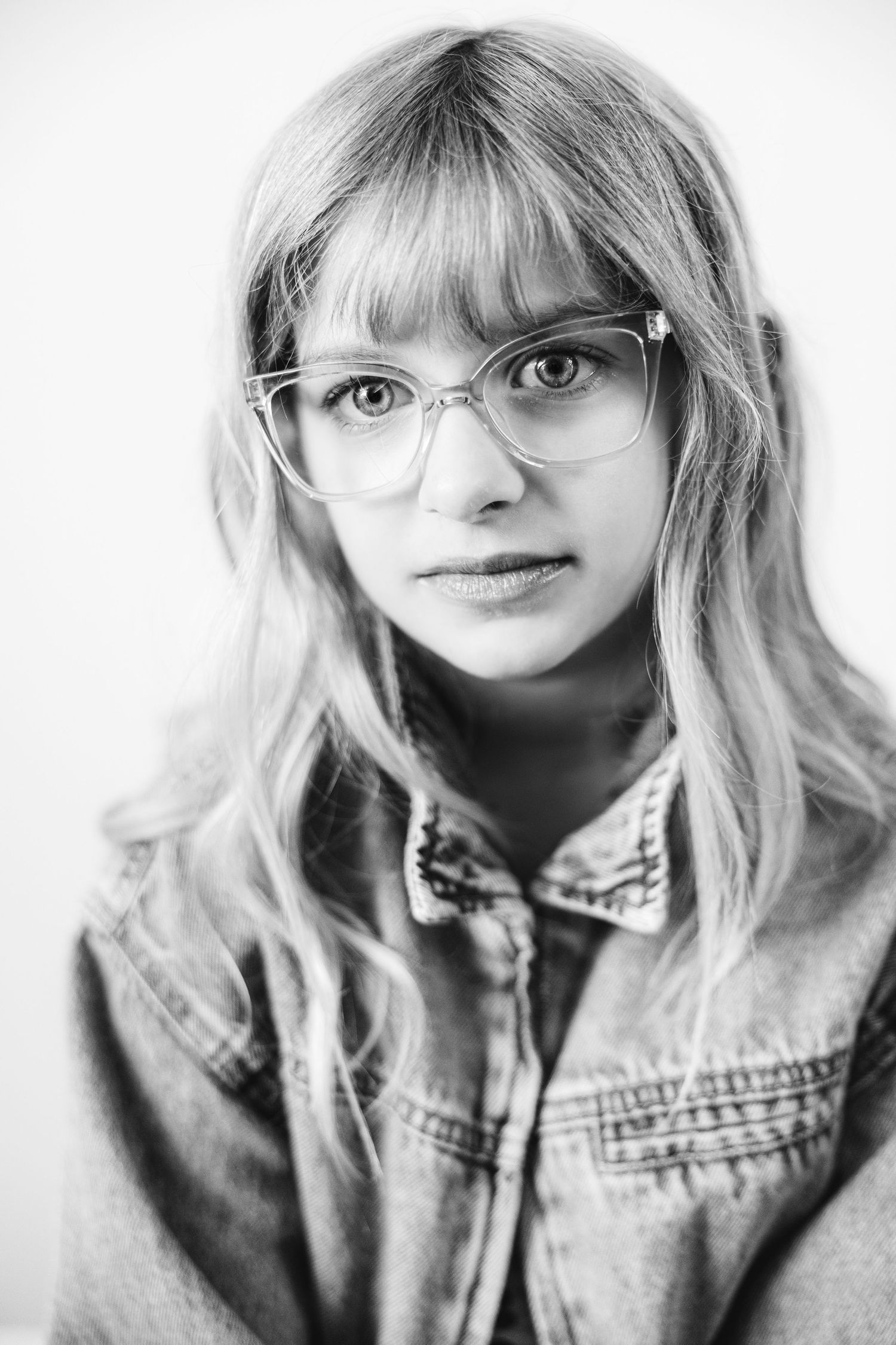 Black and white portrait of a young blonde woman wearing glasses and a denim jacket.