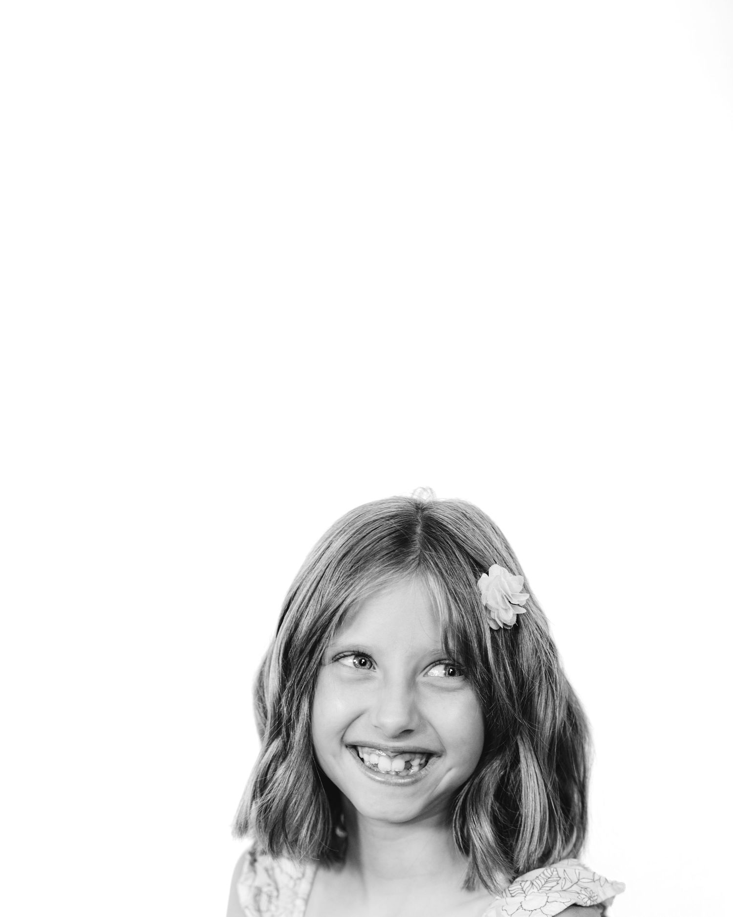 Black and white portrait of a smiling young girl with a flower hair clip showing her missing front teeth.
