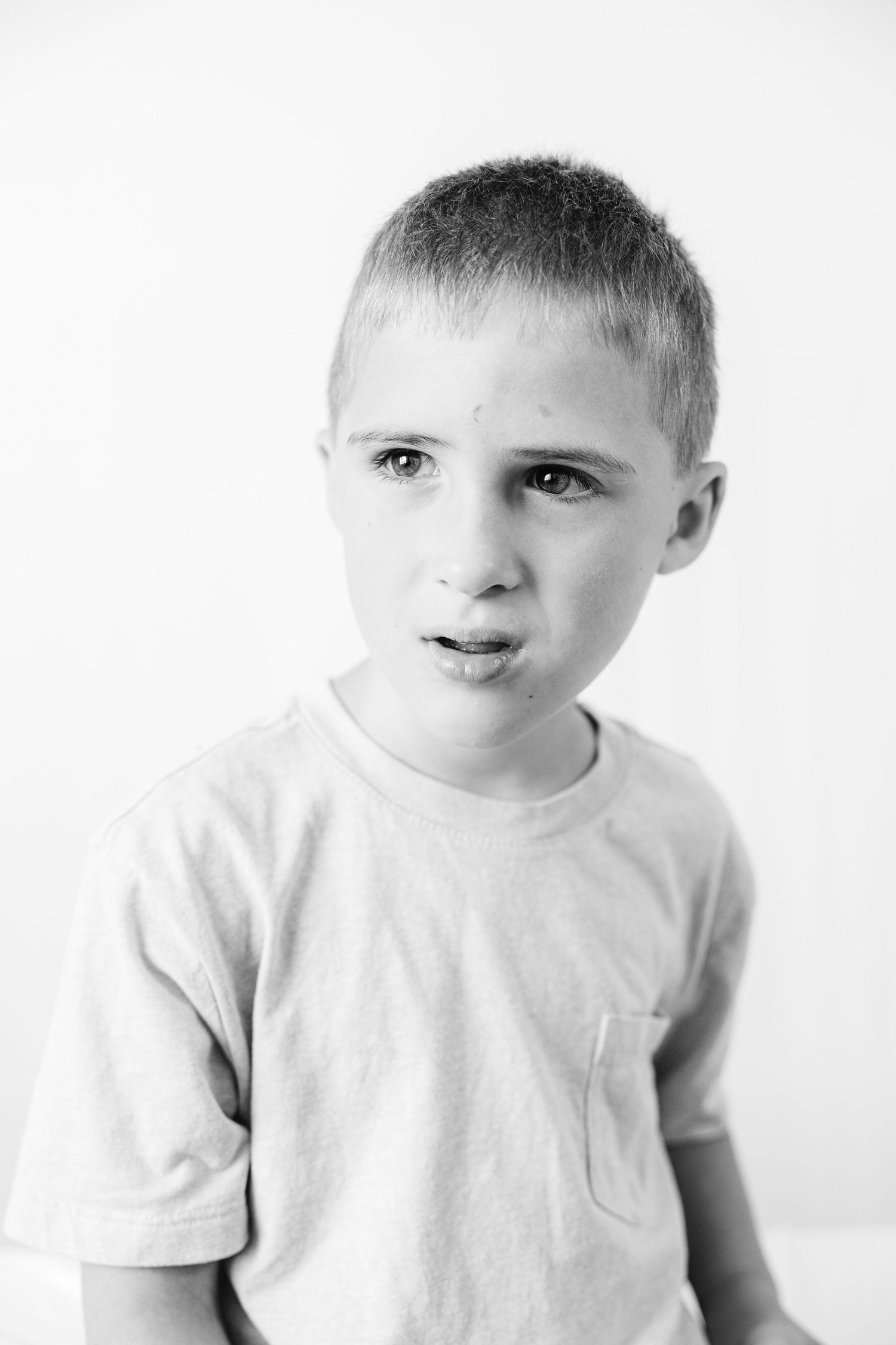 Black and white portrait of a young boy with short hair wearing a t-shirt, looking at the camera with a serious expression.