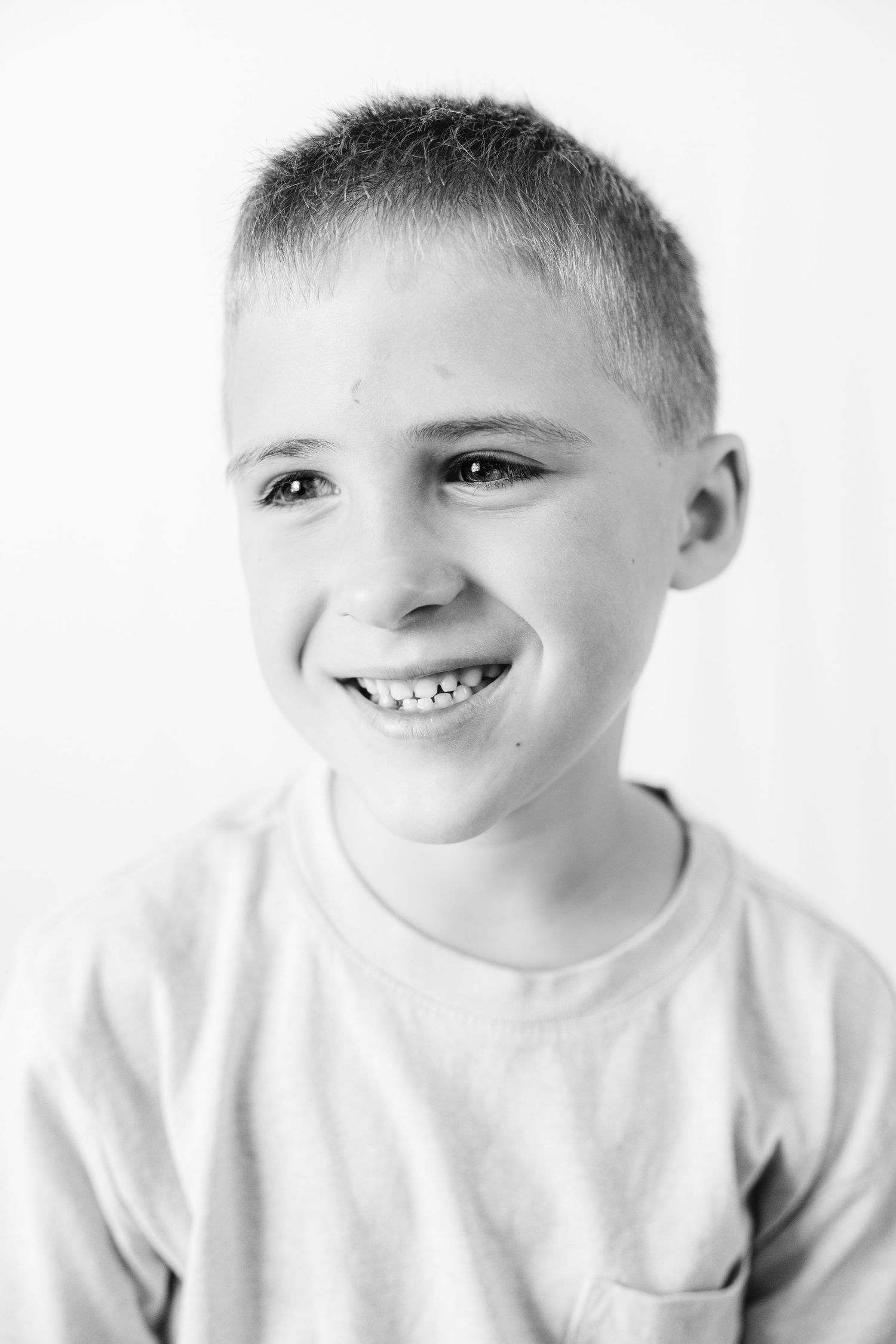 Black and white portrait of a smiling young boy with short hair wearing a t-shirt with chest pocket.