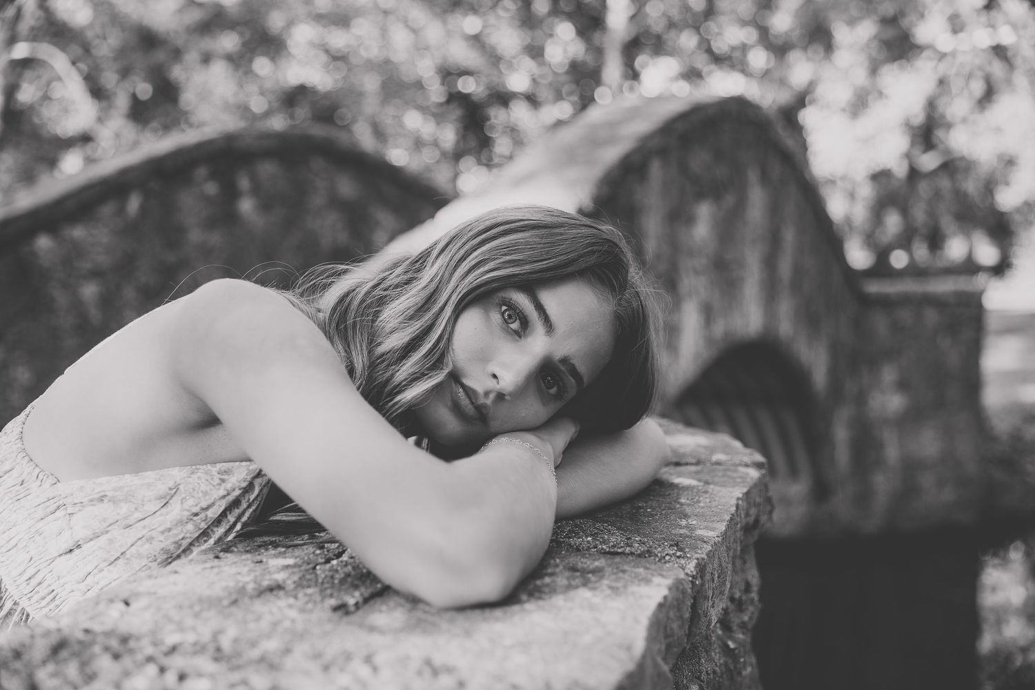 Black and white portrait of a young woman resting her head on a stone surface outdoors. Katie Chamberlain Photography