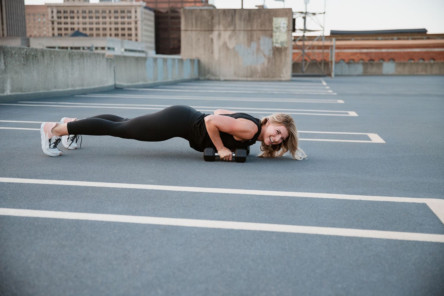 Woman in black athletic wear performing a push-up on a rooftop parking lot during an outdoor workout session. Photo by Katie Chamberlain