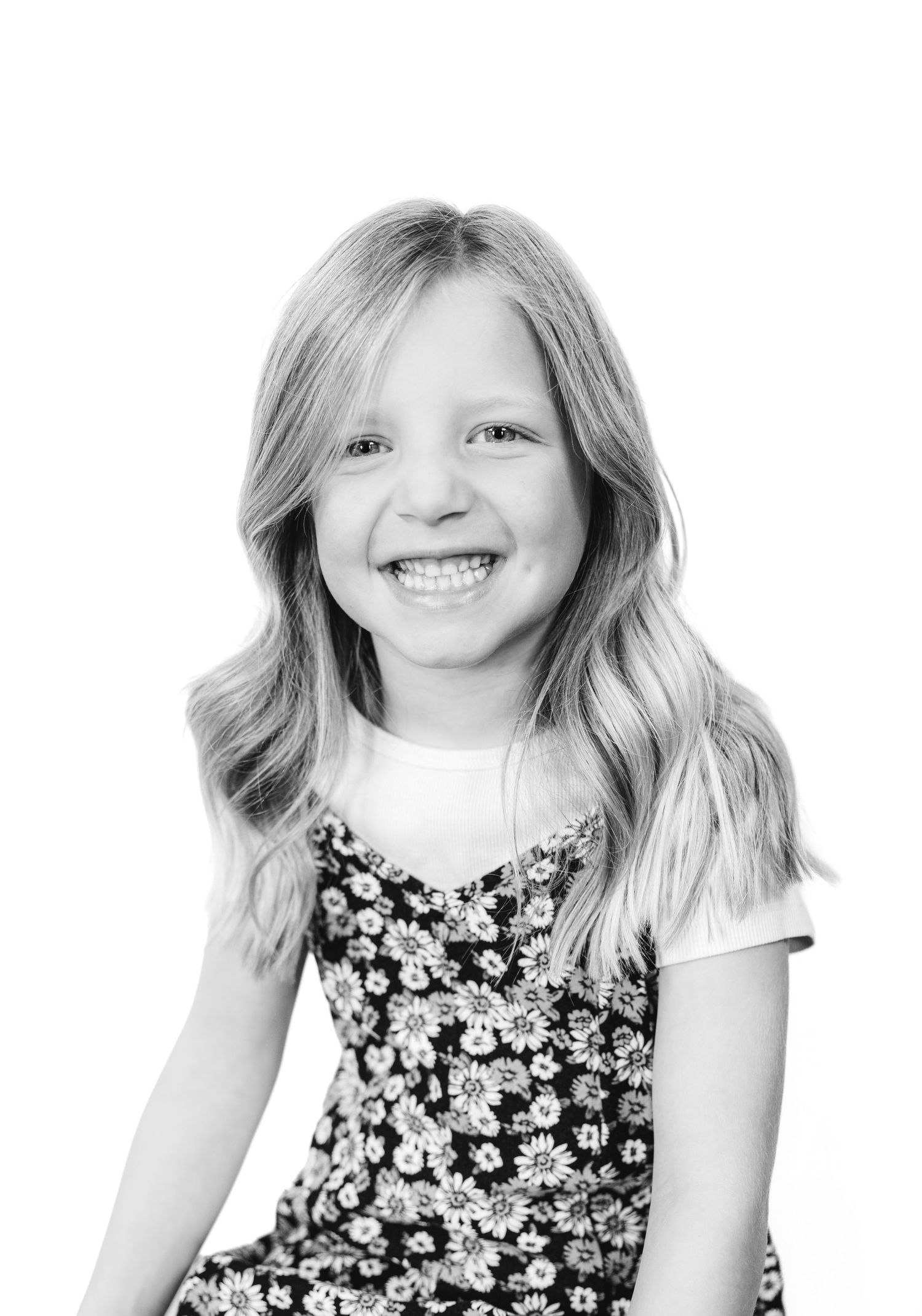 Black and white portrait of a cheerful young girl with wavy hair wearing a floral dress.